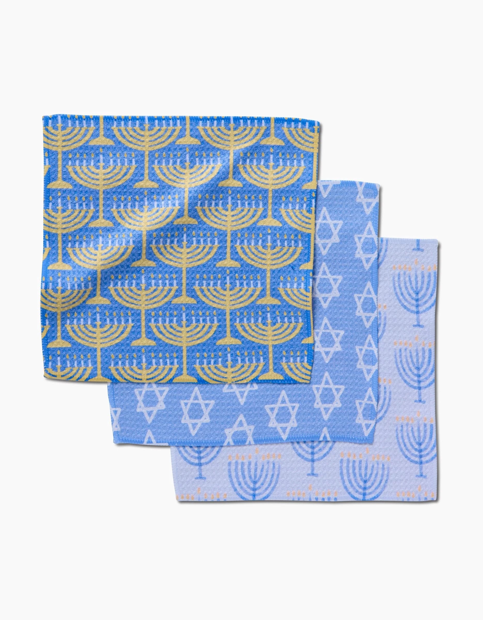 The Mindfulnice Hanukkah Lights set includes two blue kitchen tea towels: one with yellow menorahs, the other with white menorahs and Stars of David on soft light blue Geoweave fabric.