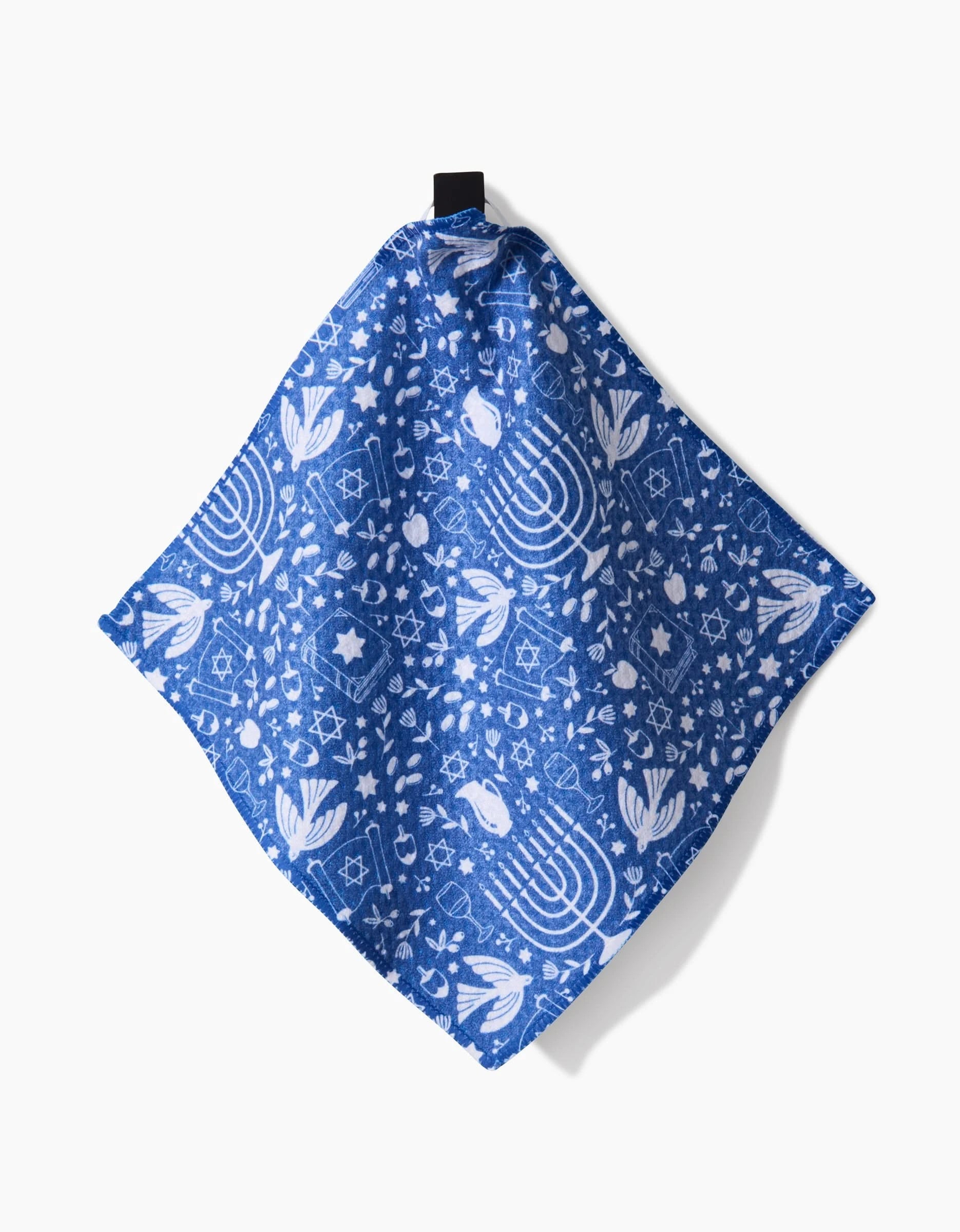 The Hanukkah Sameach blue cloth napkin by Megan Kampa features Geoweave fabric and white Hanukkah symbols, making it a festive kitchen addition. The design includes menorahs, dreidels, stars of David, and olive branches on a white background.