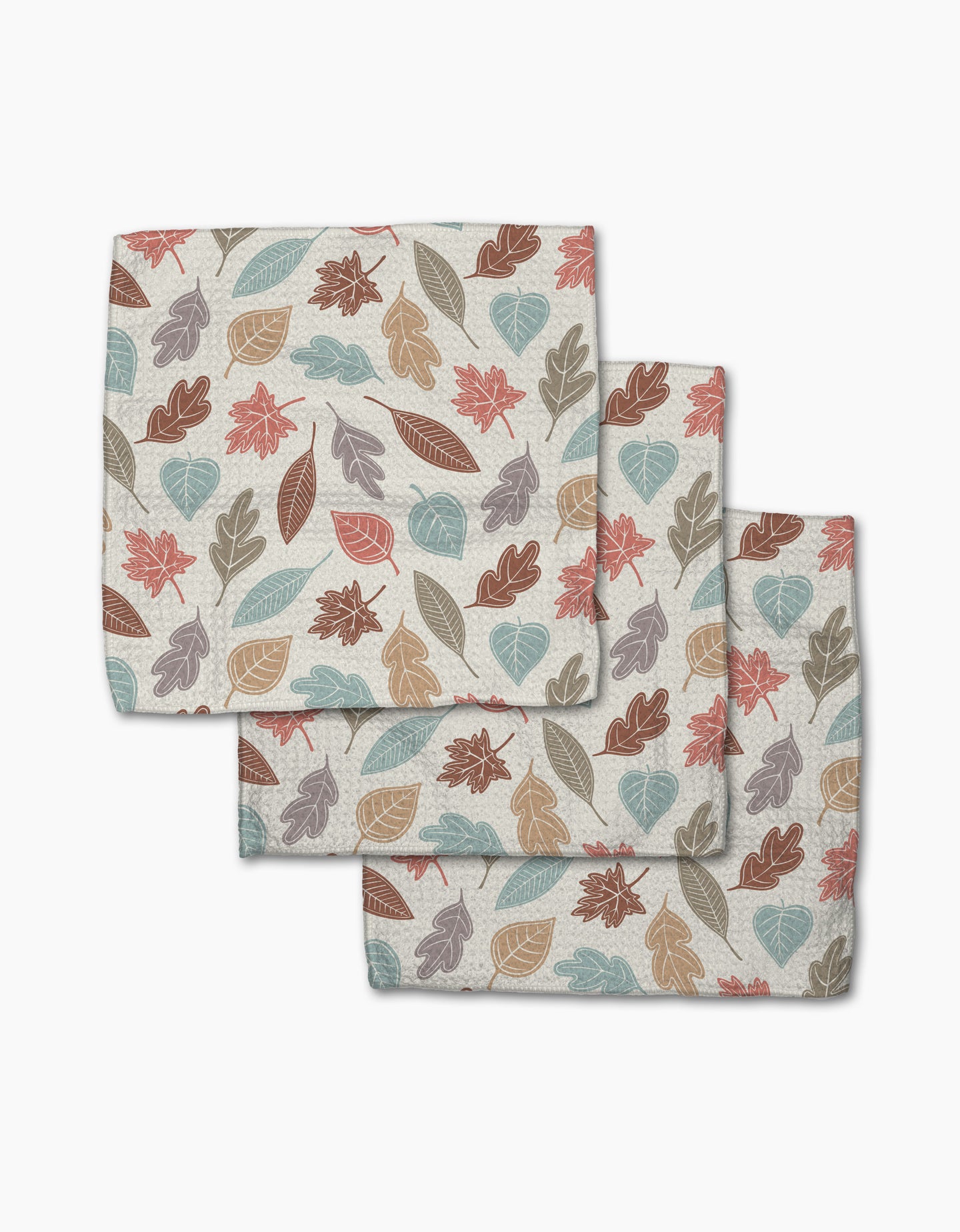 Three folded Harvest Scatter napkins by Sarah Daugherty, featuring autumn leaves in orange, brown, blue, and beige on a light background, are stacked with overlapping corners for an inviting display.