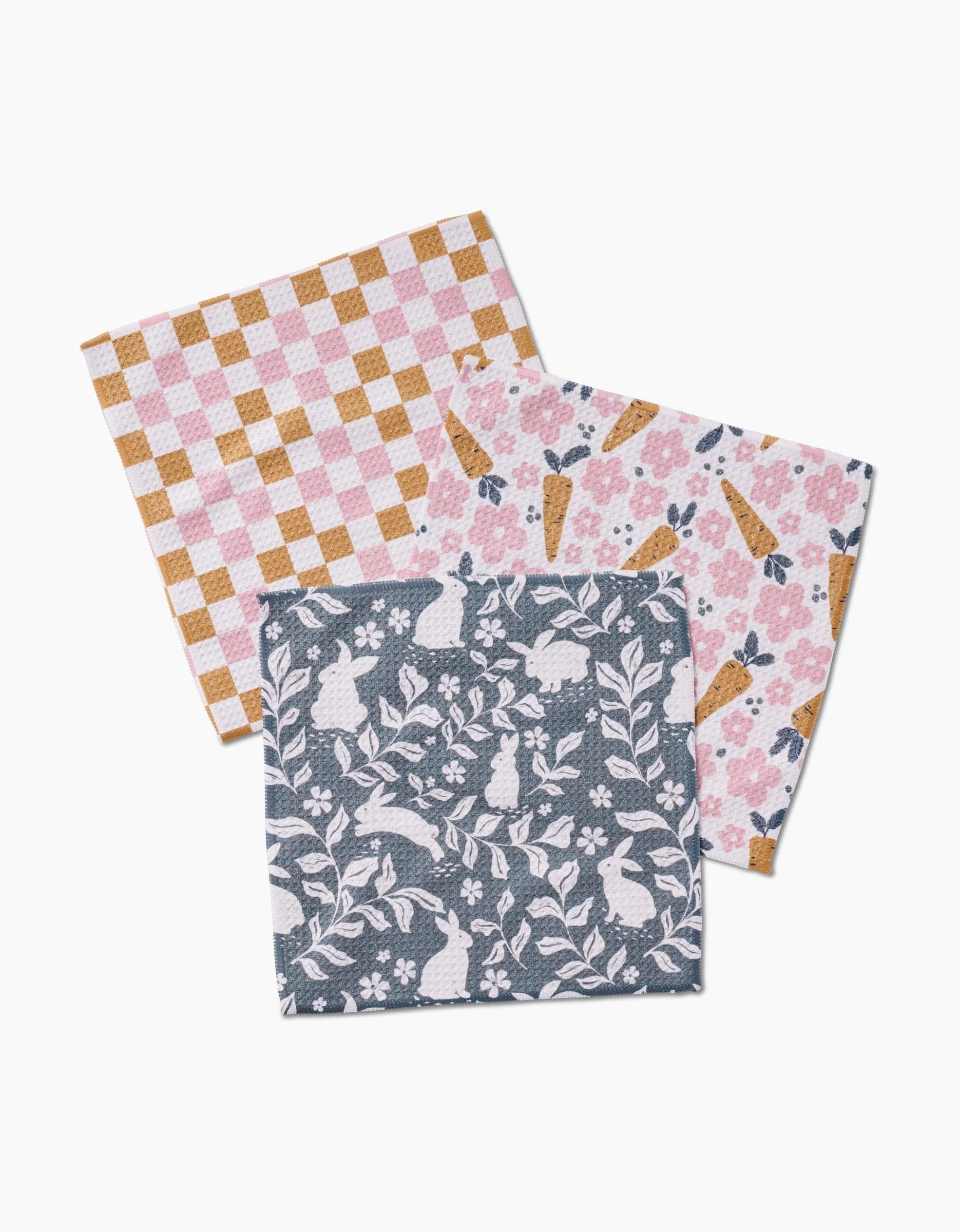 The Hippity Hop set by Charlie Rowan Designs includes three square cloth napkins made from durable Geoweave fabric, featuring pink/yellow checks, playful carrots with paw prints, and white rabbits with leaves on dark gray.