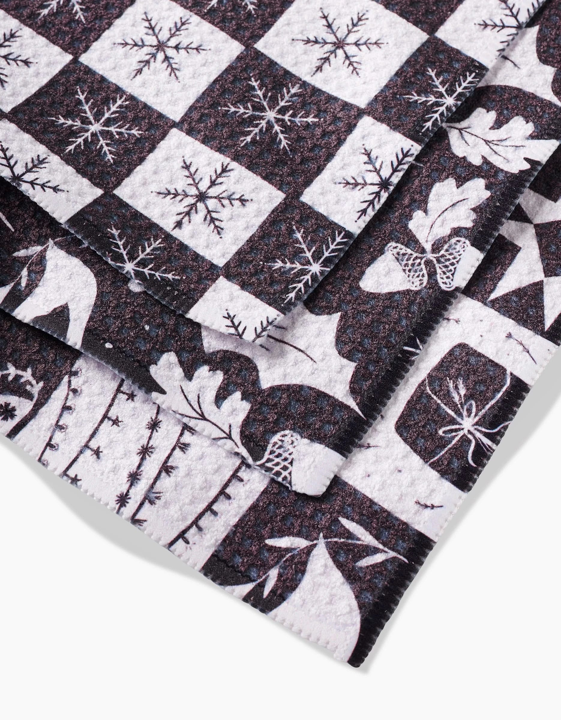 A close-up of Elana Gabrielles Holiday Love shows eco-friendly Geoweave fabric with a checkered pattern of snowflakes, holly leaves, reindeer, and wrapped gifts in white and dark brown for festive charm.