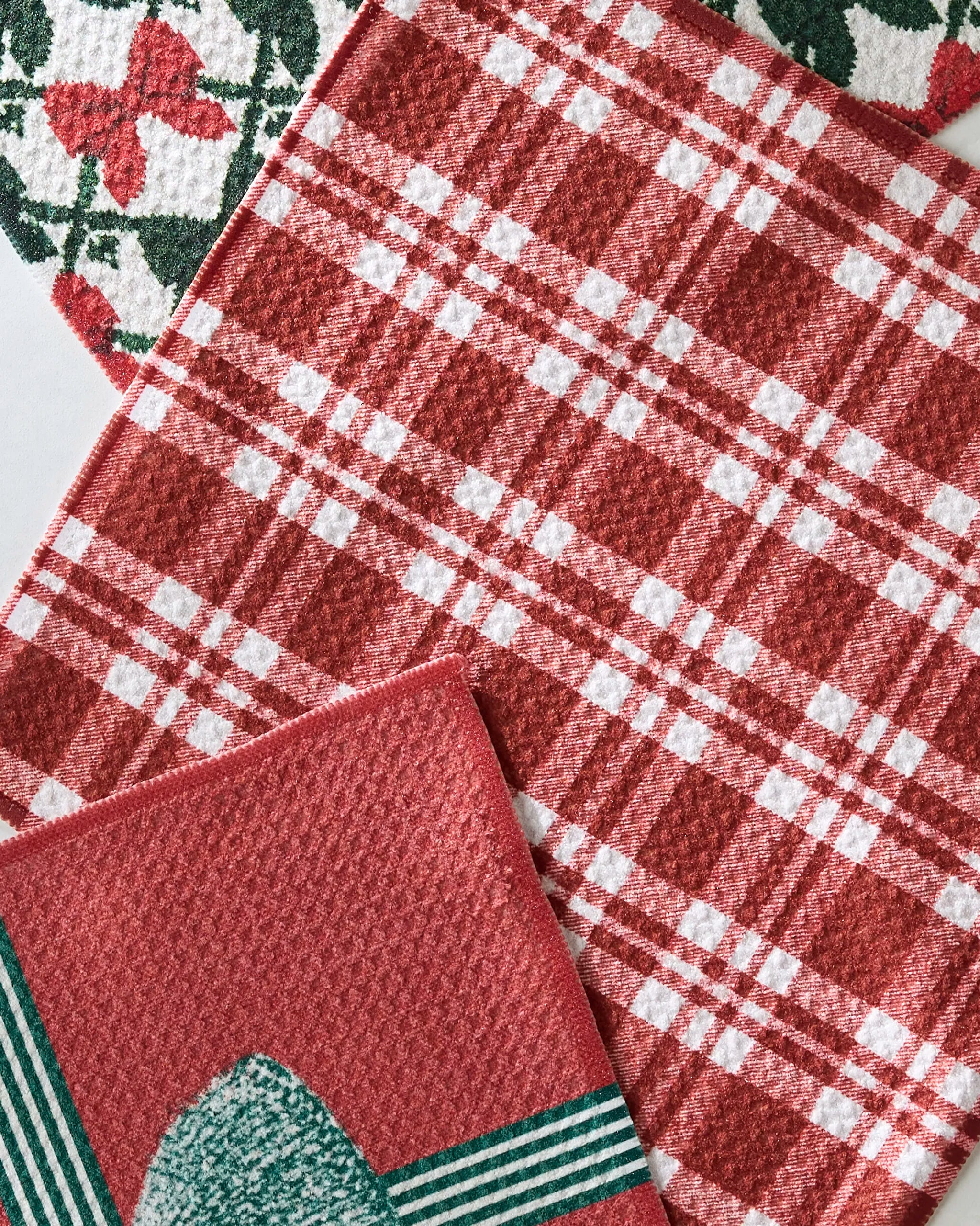Three Geometry Hollis kitchen towels are shown: an absorbent, recycled set including a red and white plaid, a geometric design, and a holly leaf pattern.