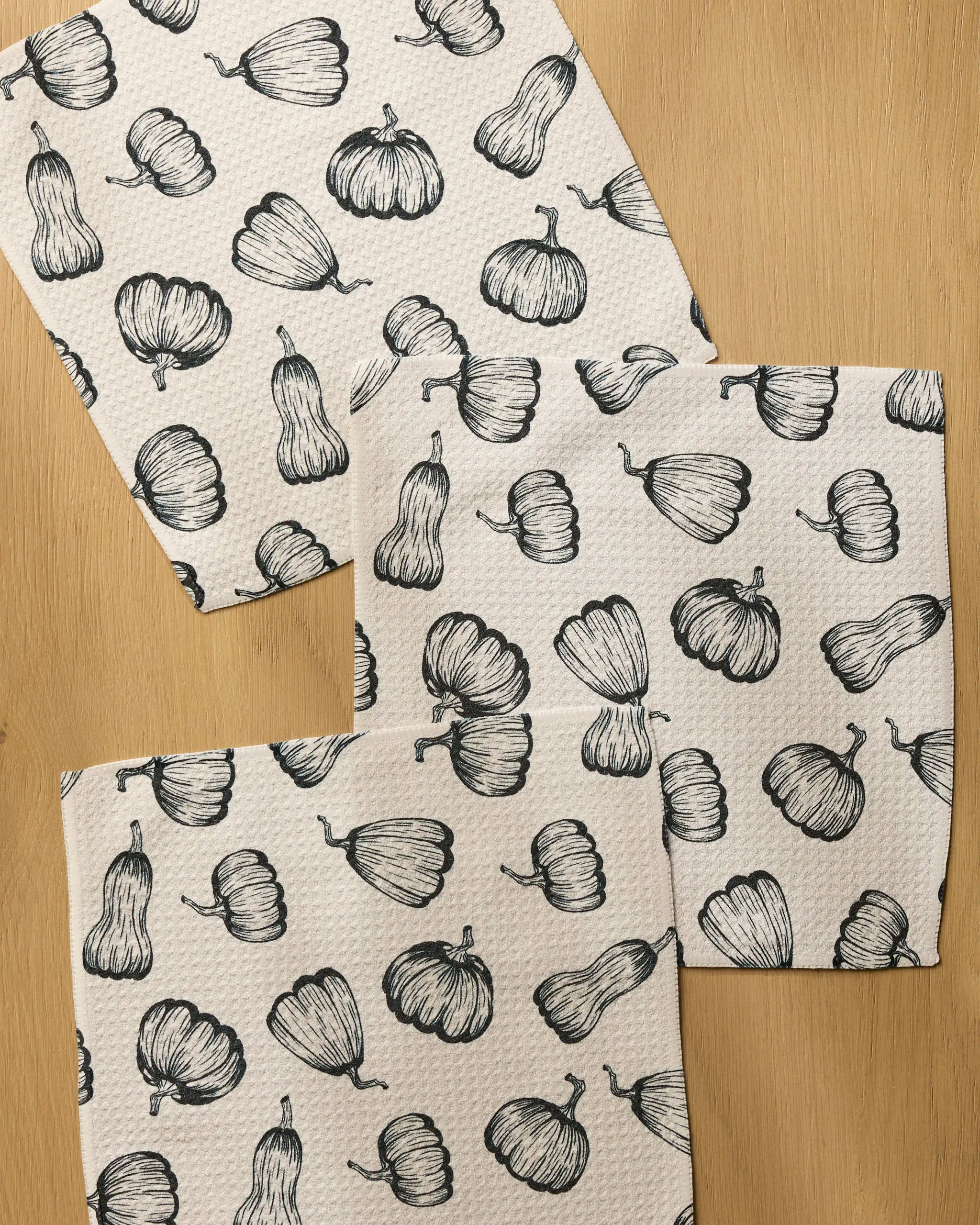 The Geometry Hollow Season dishcloth set includes four absorbent white towels, each decorated with black line art of pumpkins and gourds repeated across the surface.