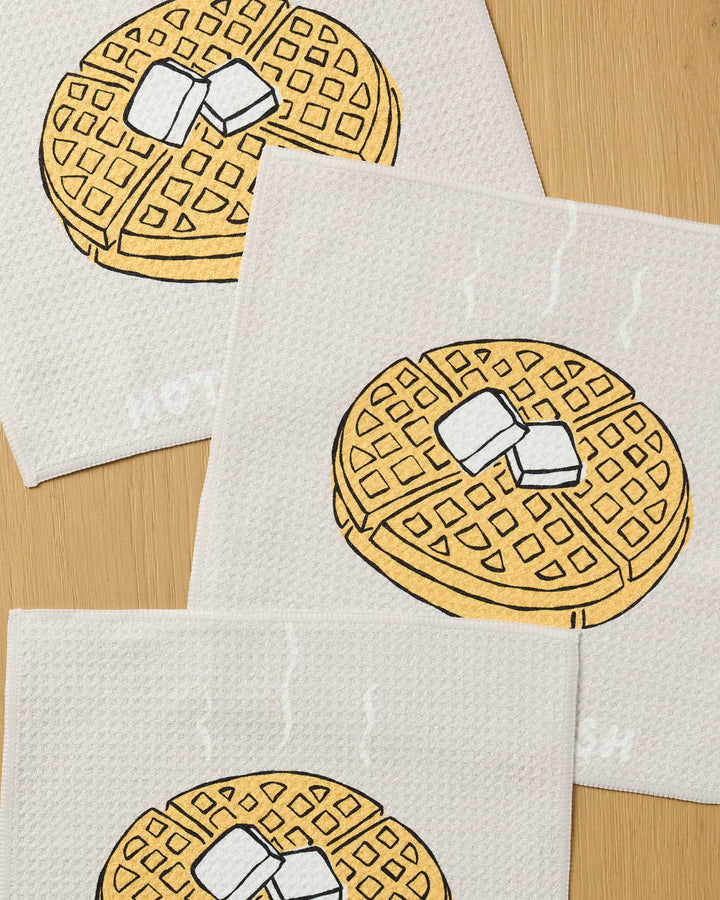 The "Hot and Fresh" cloth napkins by Rosa Kichline are made from recycled materials and feature illustrations of steaming waffles with melting butter on a wooden surface.