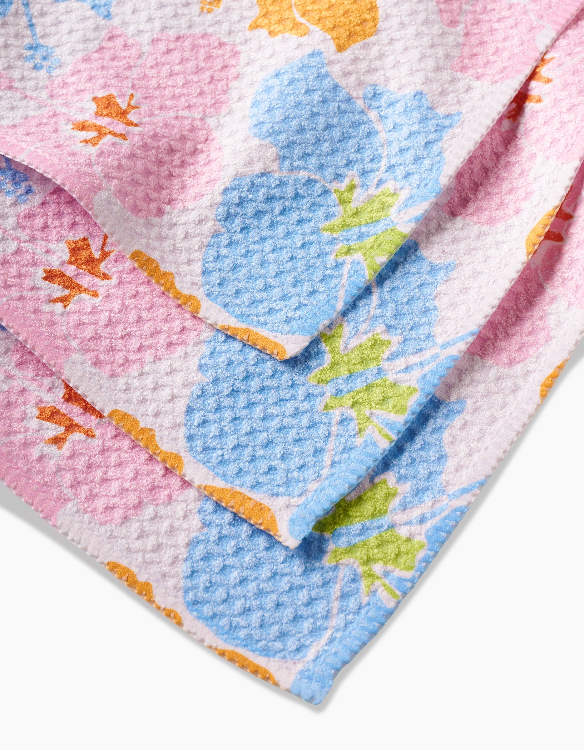 A close-up of the Hula Hues dishcloth by GEOMETRY, featuring a textured waffle weave and pastel floral prints in pink, blue, orange, and green on recycled material.