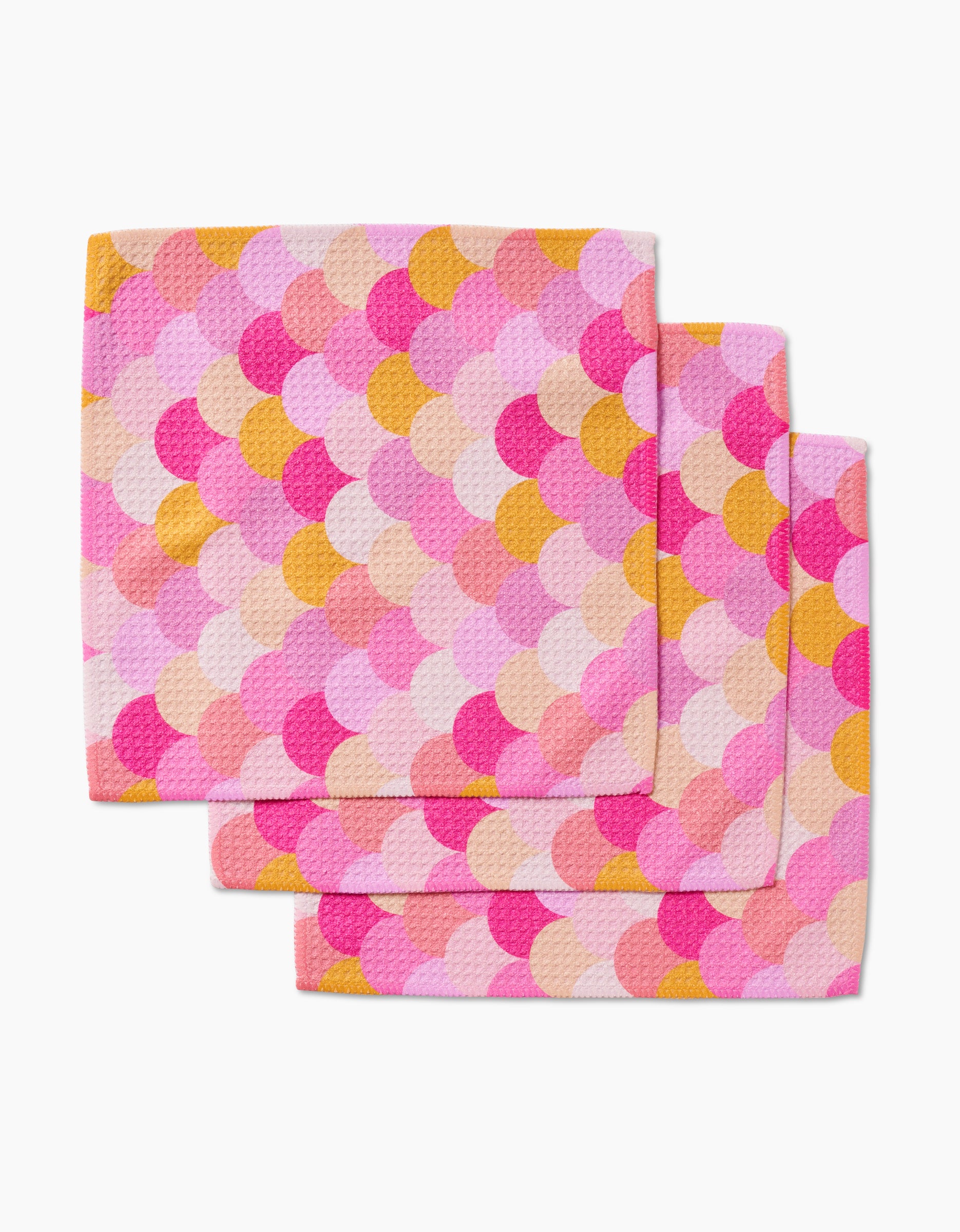 GEOMETRY’s Inherit set includes three reusable cloths made from Geoweave fabric, each with a colorful scallop pattern in pink, peach, yellow, and orange on a white background.