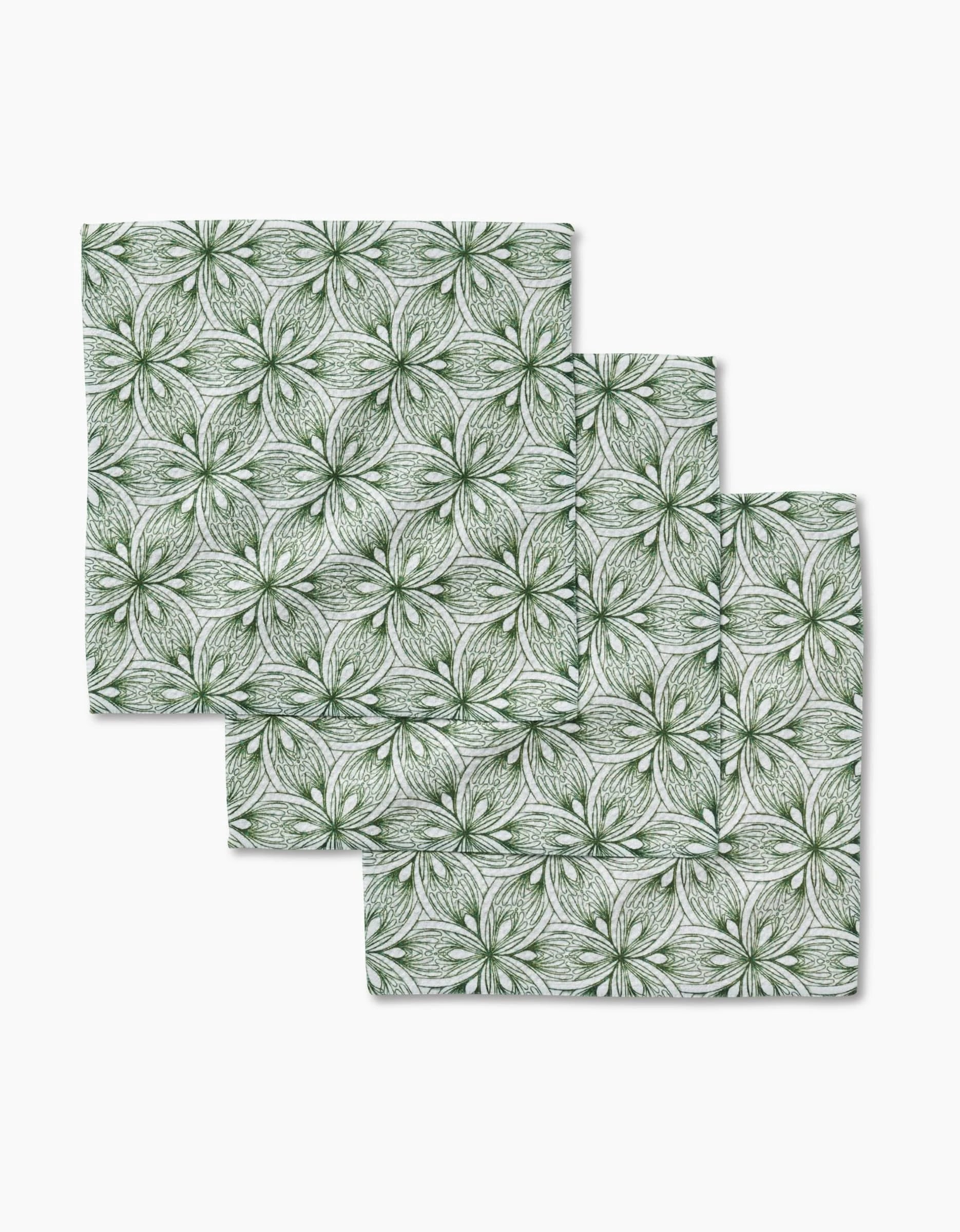 Three Interlaced Petals square napkins by Marta Harvey, made from recycled materials, display a green and white geometric floral pattern and are arranged in an overlapping stack on a white background.