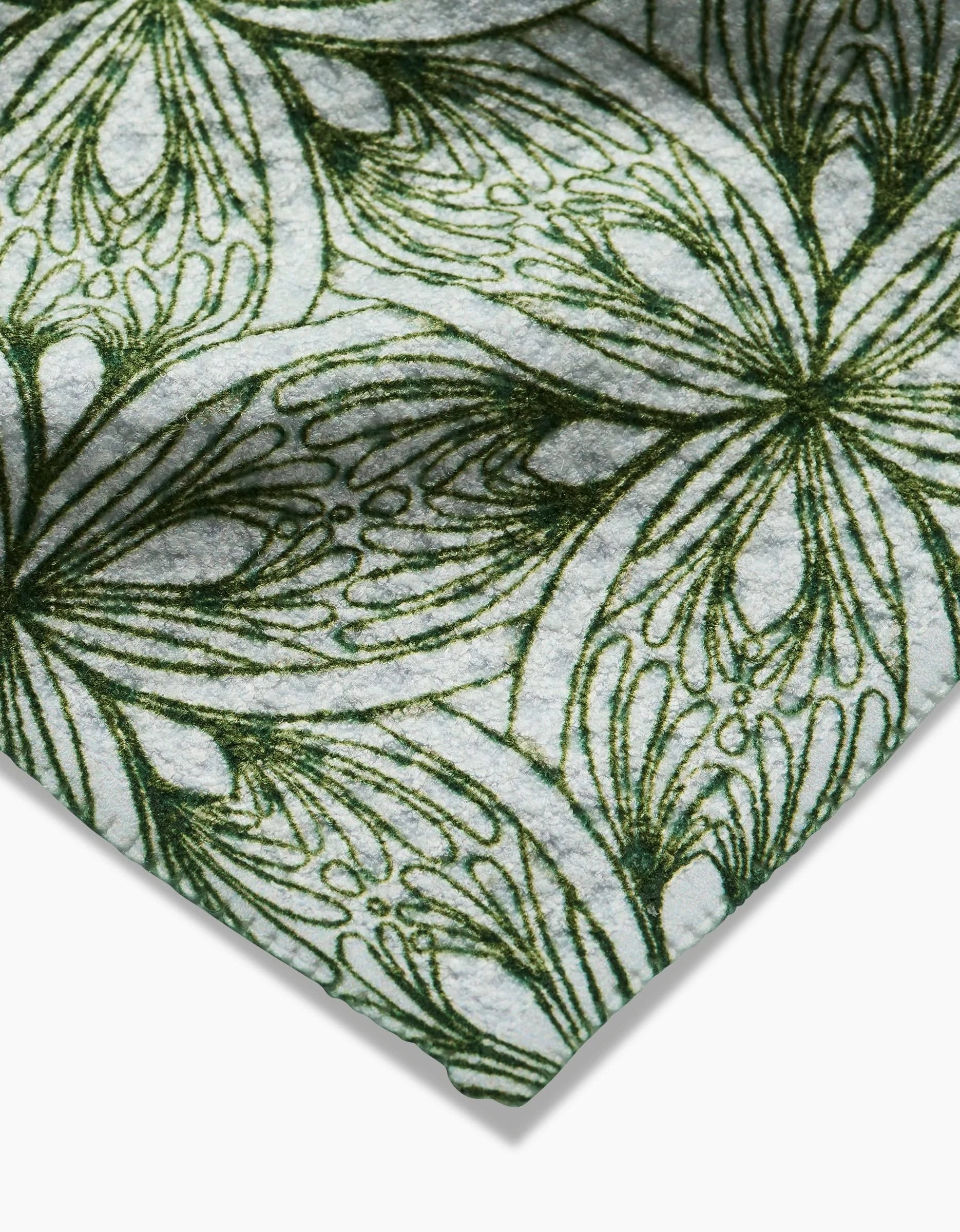 A close-up of the Interlaced Petals dishcloth by Marta Harvey, showcasing a super-absorbent cloth with a green, artistic floral pattern on white—layered and swirling lines form an intricate organic design.