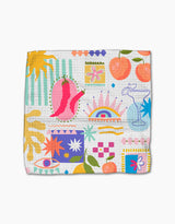 The Italian Picnic dishcloth set by Marina Solodka features vibrant illustrations—pink chili peppers, peaches, a margarita glass, eyes, sunbursts, and geometric patterns—on recycled materials with a white background.