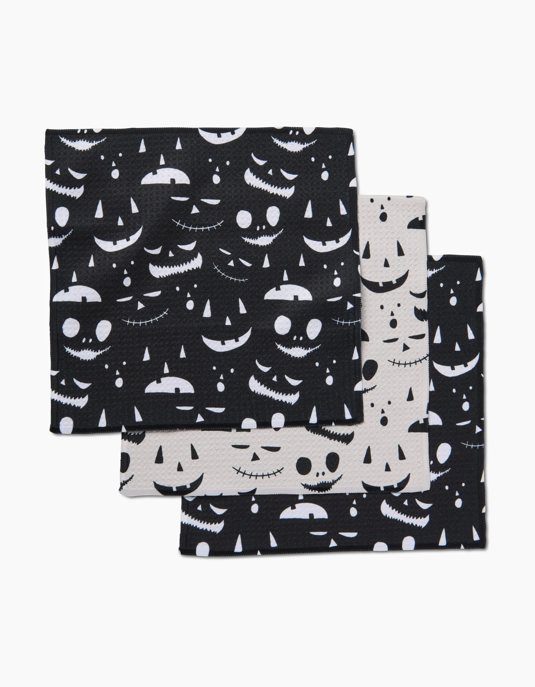 The Jack O Lantern Jamboree dishtowel set by Danelys Sidron includes three super-absorbent, recycled rectangular cloths with black and white backgrounds, each featuring spooky jack-o-lantern faces. Towels are stacked and slightly overlapping.