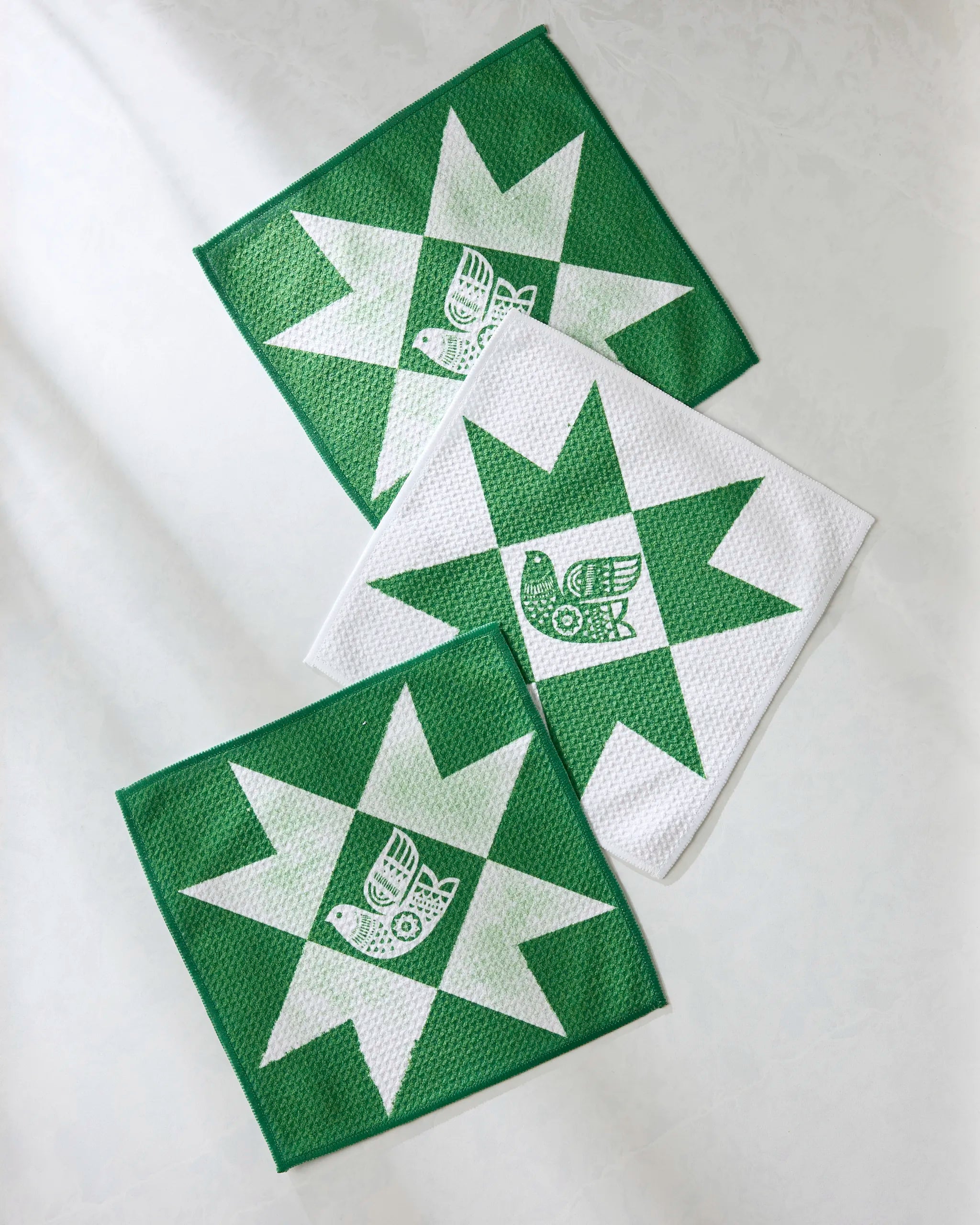 The Geometry Joybird set features three reusable dishcloths with a green and white star pattern and a stylized bird in the center, arranged overlapping on a light surface—an eco-friendly kitchen towel option for any home.