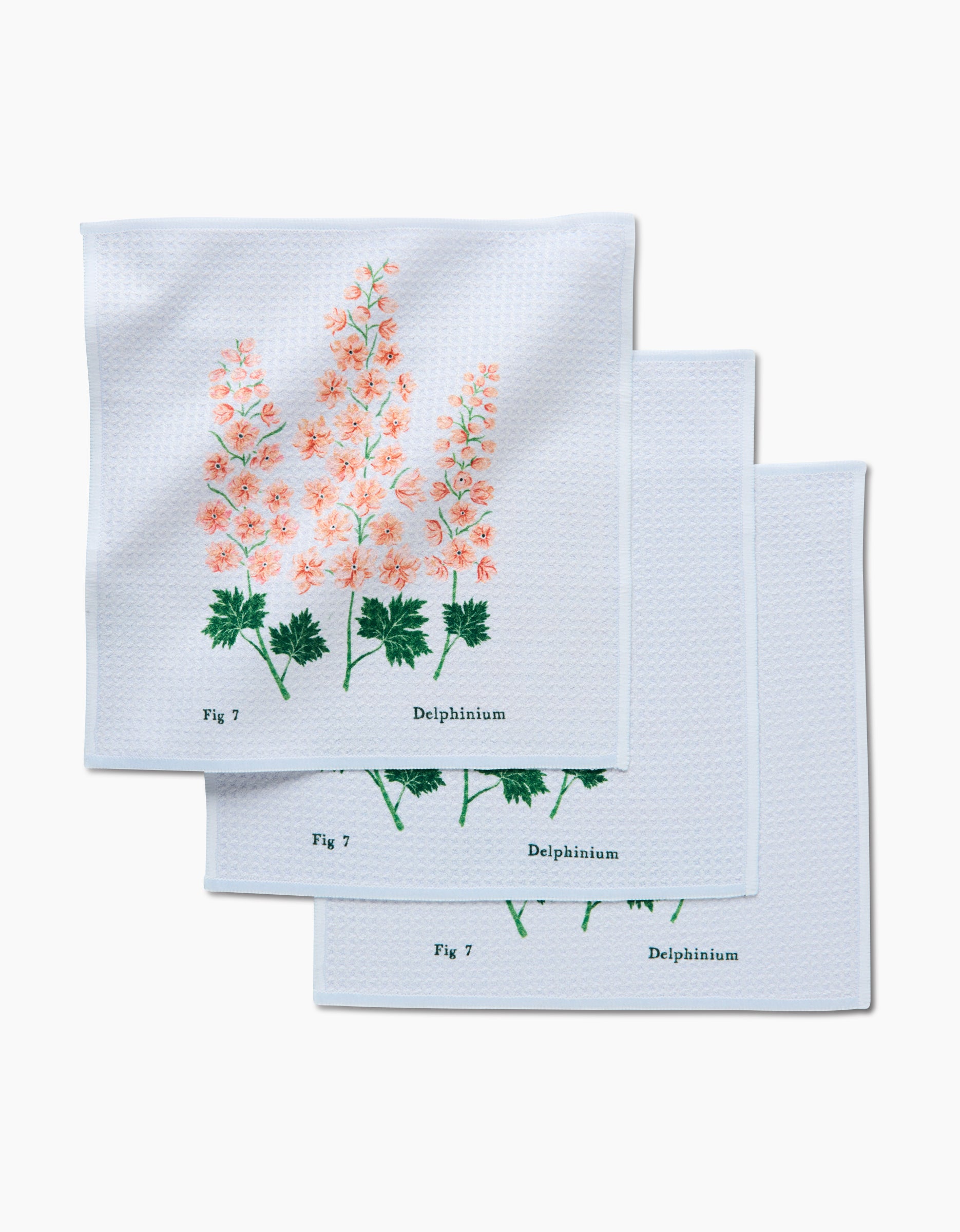 The Linda Fox July Delphinium set includes three white dishcloths made from recycled materials, each featuring pink delphiniums, green leaves, and black Fig 7 and Delphinium text aligned with the floral design.
