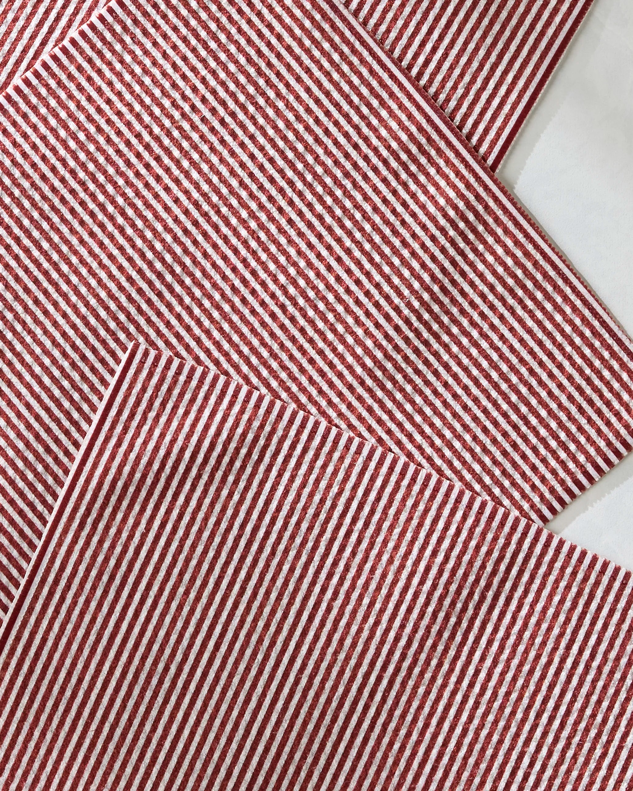 Geometry’s Kringle placemats, made from recycled materials, feature red and white stripes and are stylishly arranged in an overlapping pattern on a white surface for a neat, eye-catching display.