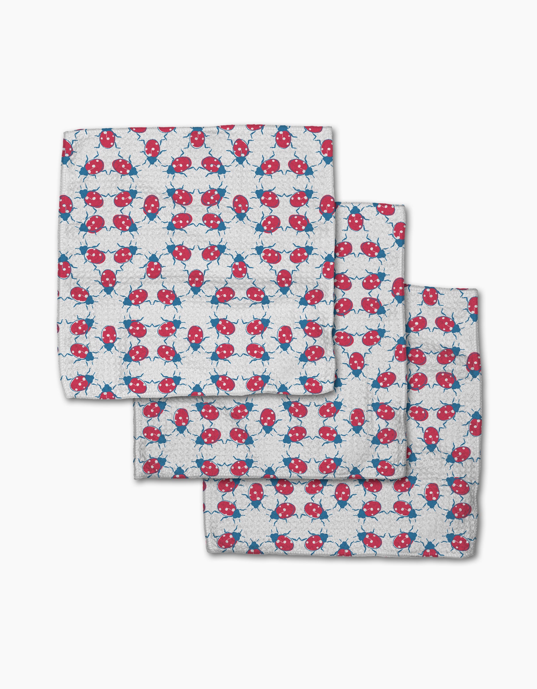 Three white dishcloth napkins from Second Nature Studio’s Ladybug Dance, made with Geoweave fabric and featuring a playful pattern of red and blue ladybugs and blue geometric stars, are shown slightly overlapping on a white background.