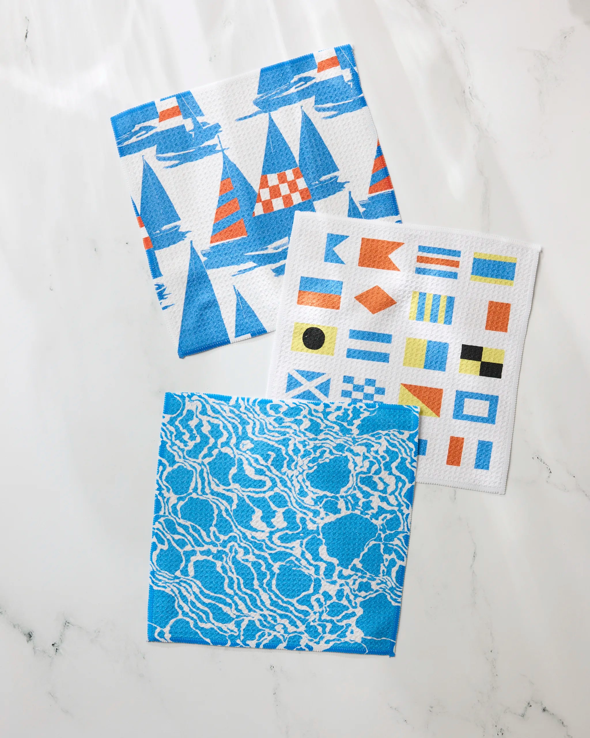 Geometry's Leeward dishcloth set features three absorbent cloths: blue and orange sailboats, colorful nautical flags, and blue-and-white water ripples—perfect for any kitchen.