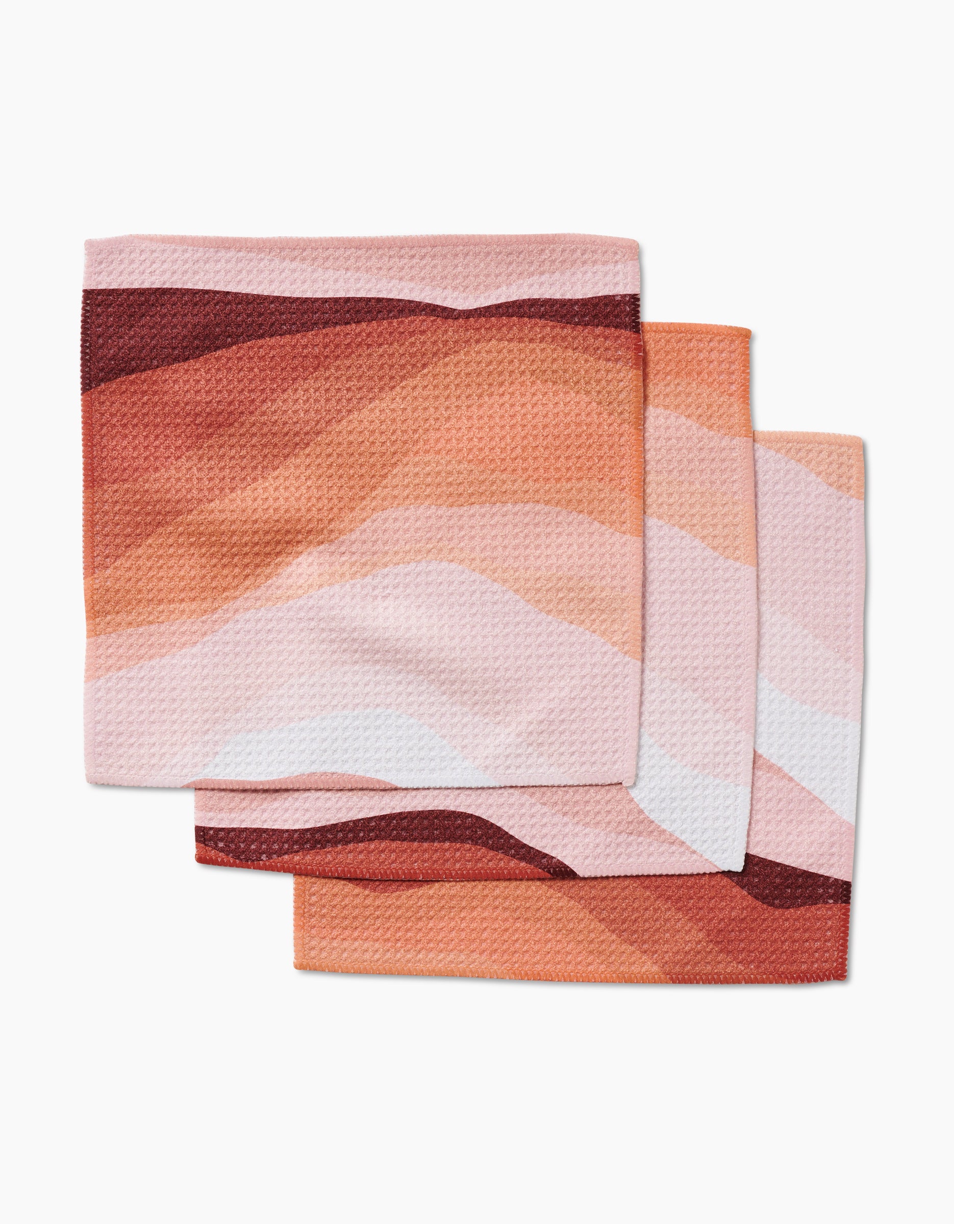 Three folded GEOMETRY Levels of Fall cloth napkins, crafted from super-absorbent Geoweave™ fabric with an abstract wavy pattern in pink, orange, red, and white, are stacked with slight overlap on a white background.
