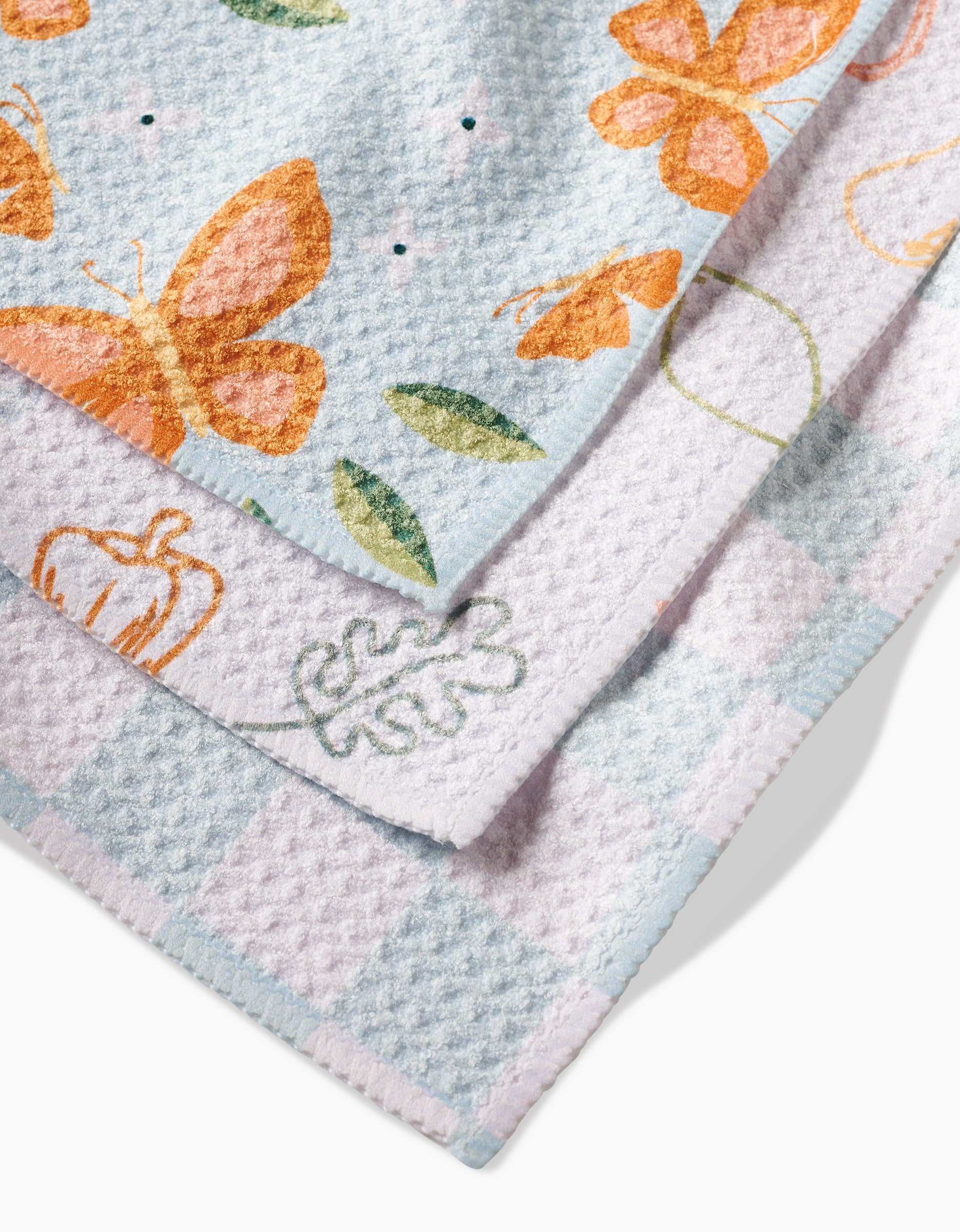 Three textured dishcloths from Sweet Simple Vegans Life is Beautiful set are layered: the top has orange butterflies and green leaves, the middle features pumpkins and leaves, and the bottom shows a blue and white checkered pattern with leaves—all made from recycled materials.