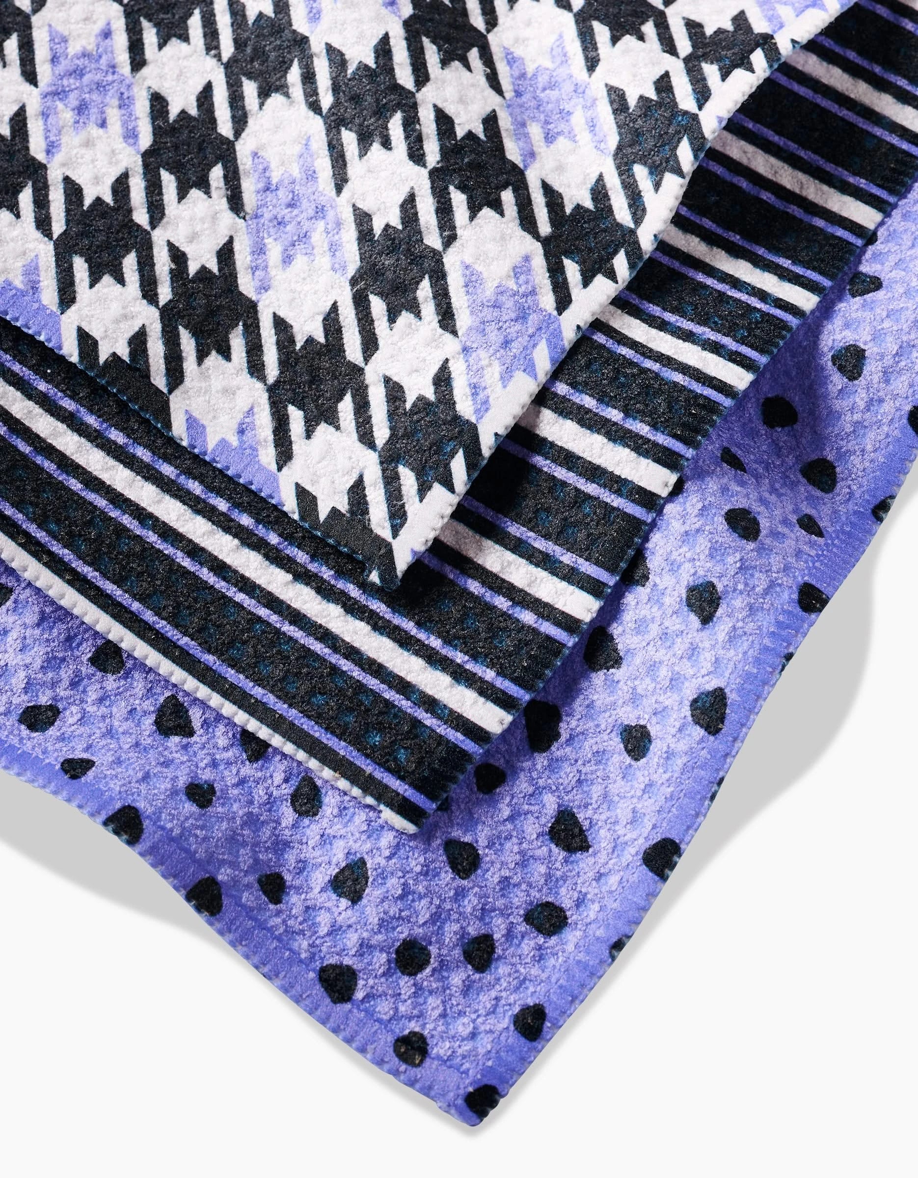 Lilac Schemes by Hufton Studio features three Geoweave dishcloths layered together: black-and-white houndstooth, black-and-white stripes, and black polka dots on purple—durable and stylish for your kitchen.