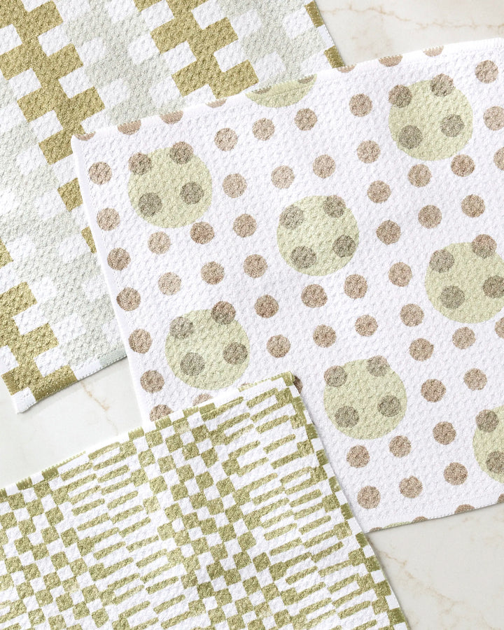 The Studio Jeannot Lotty set features three recycled dishcloths with geometric patterns—gold/white crosses, gold/beige dots, and green/white stripes—stylishly arranged on a light surface.