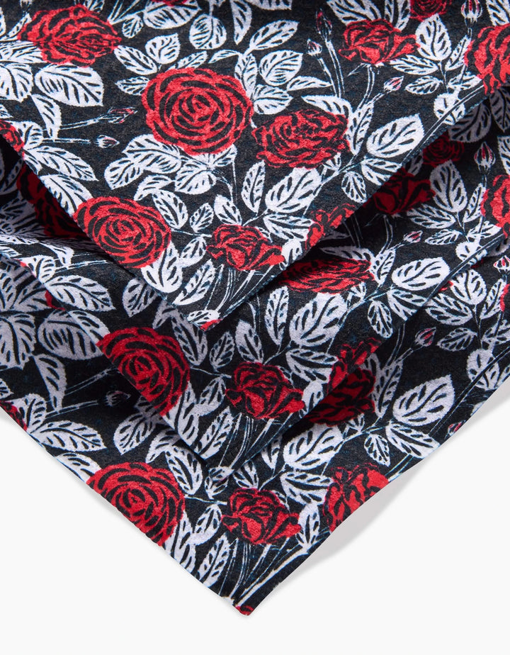 A close-up of the Love and Roses dishcloth set by Charlie Rowan Designs shows vibrant red roses and white leaves on black. Made from recycled materials, this bold set features dense, overlapping florals for a stylish touch.