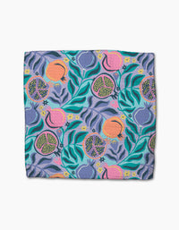 The Lucky Pomegranate dishcloth by Masha Volnova features a folded, absorbent design with vibrant pomegranates, seeds, and green leaves on a blue and purple background.