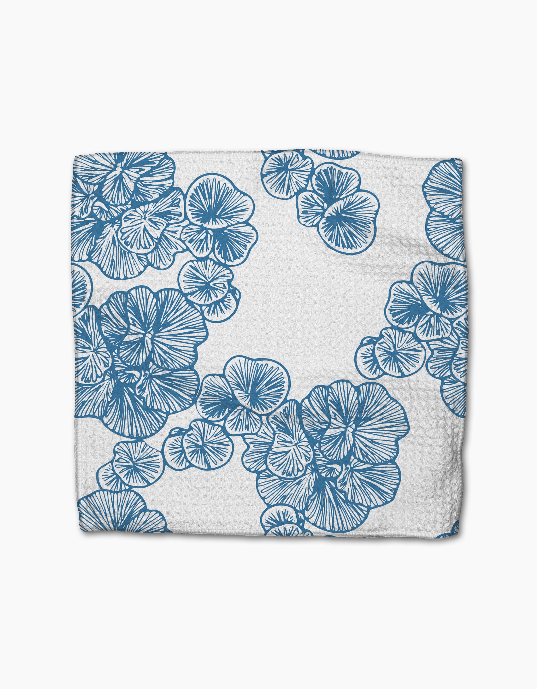 The Meadowline napkin by Second Nature Studio is a white Geoweave cloth featuring blue, intricately drawn flowers and leaves arranged diagonally across the fabric.