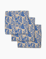 Three Mediterranean Pour beige cloth napkins by Lisa Nelson, crafted from recycled materials and featuring a blue line art pattern of vases, pomegranates, and leafy branches, shown overlapping on a white background.