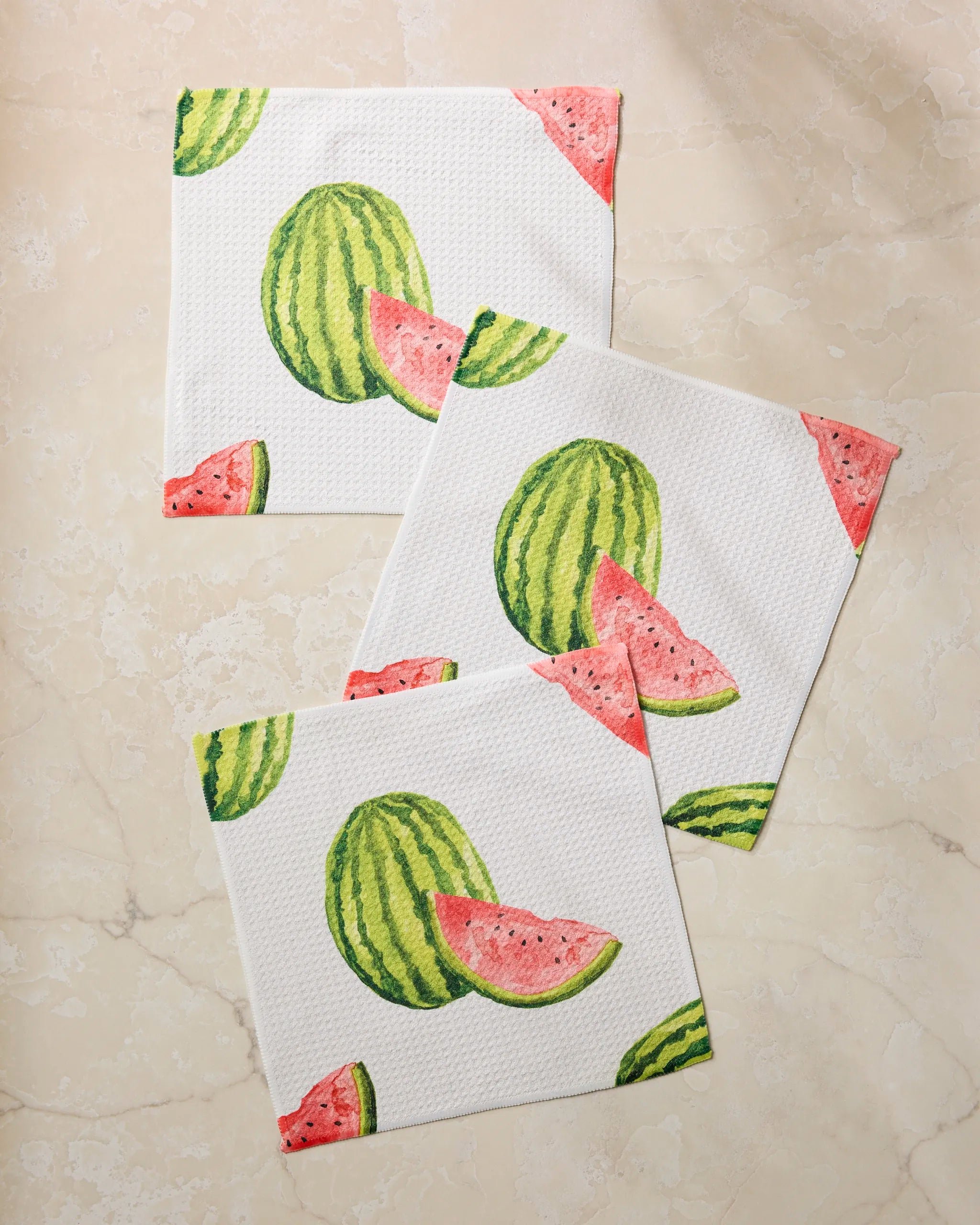 Three "Melon Market" kitchen towels by Geometry, featuring waffle texture and colorful watermelon designs, are arranged on a light marble surface.