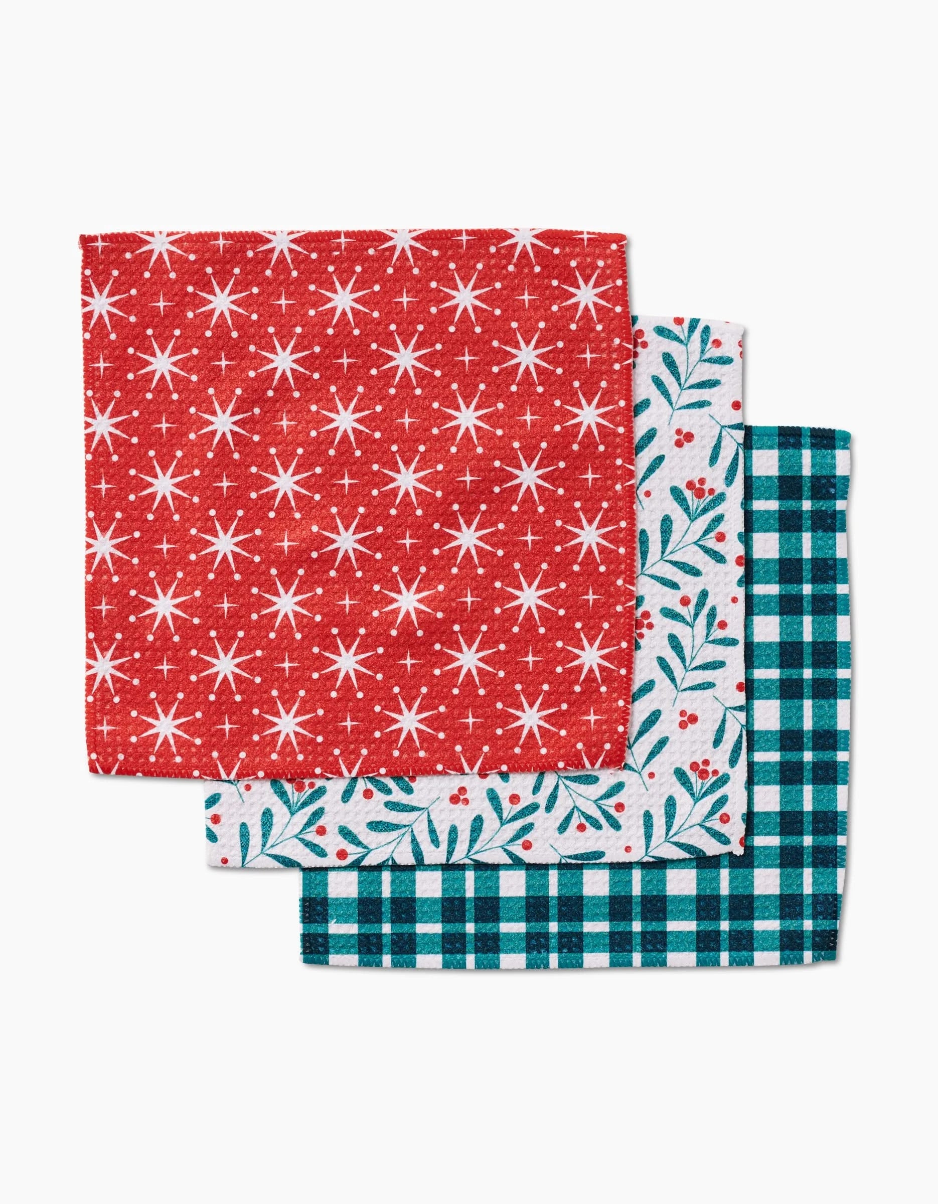 The Merry Berry napkin set by Charlie Rowan Designs includes three recycled-material napkins in unique patterns: red with white stars, white with green leaves and red berries, and blue-green plaid.