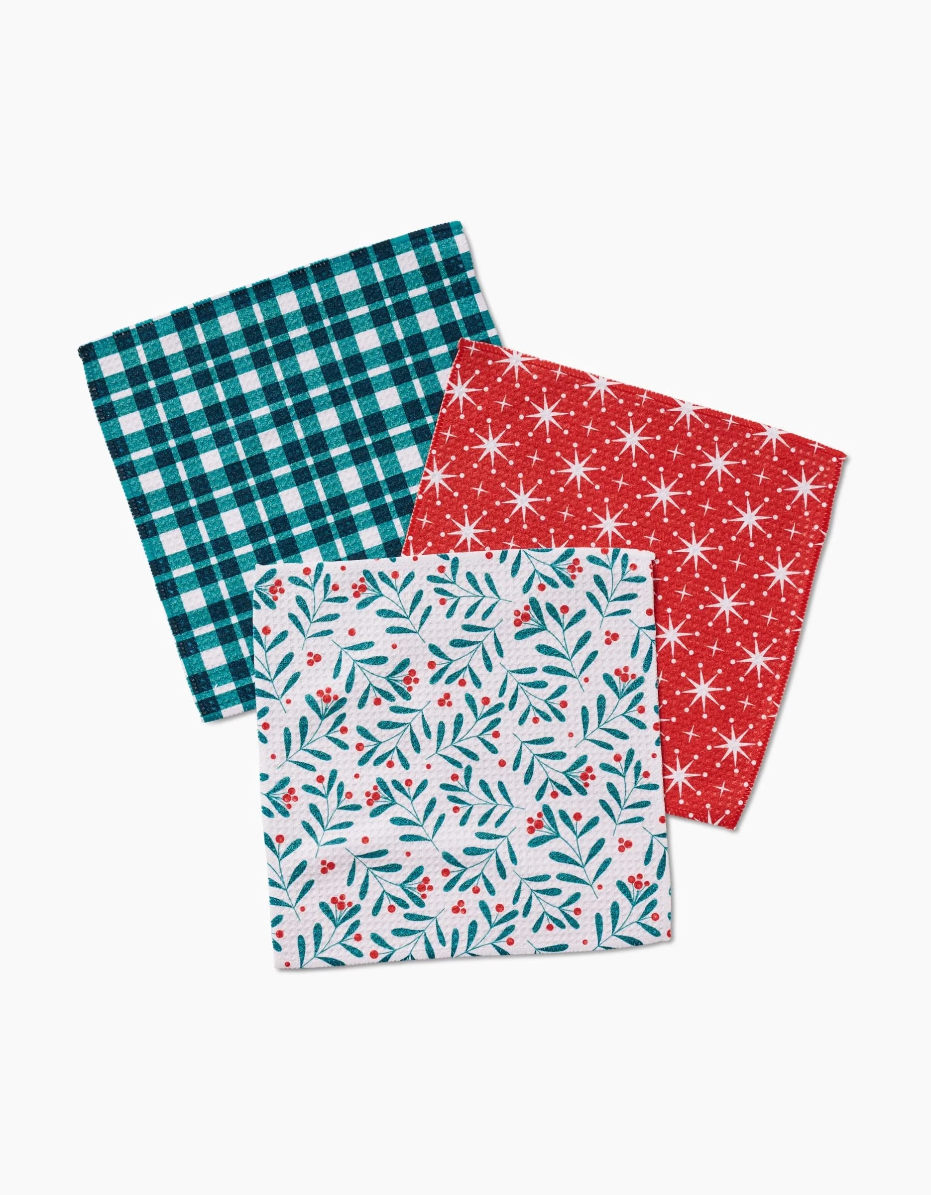 The Merry Berry napkin set by Charlie Rowan Designs includes three recycled fabric napkins: a blue and black plaid, a red with white starbursts, and a white with green leaves and red berries.