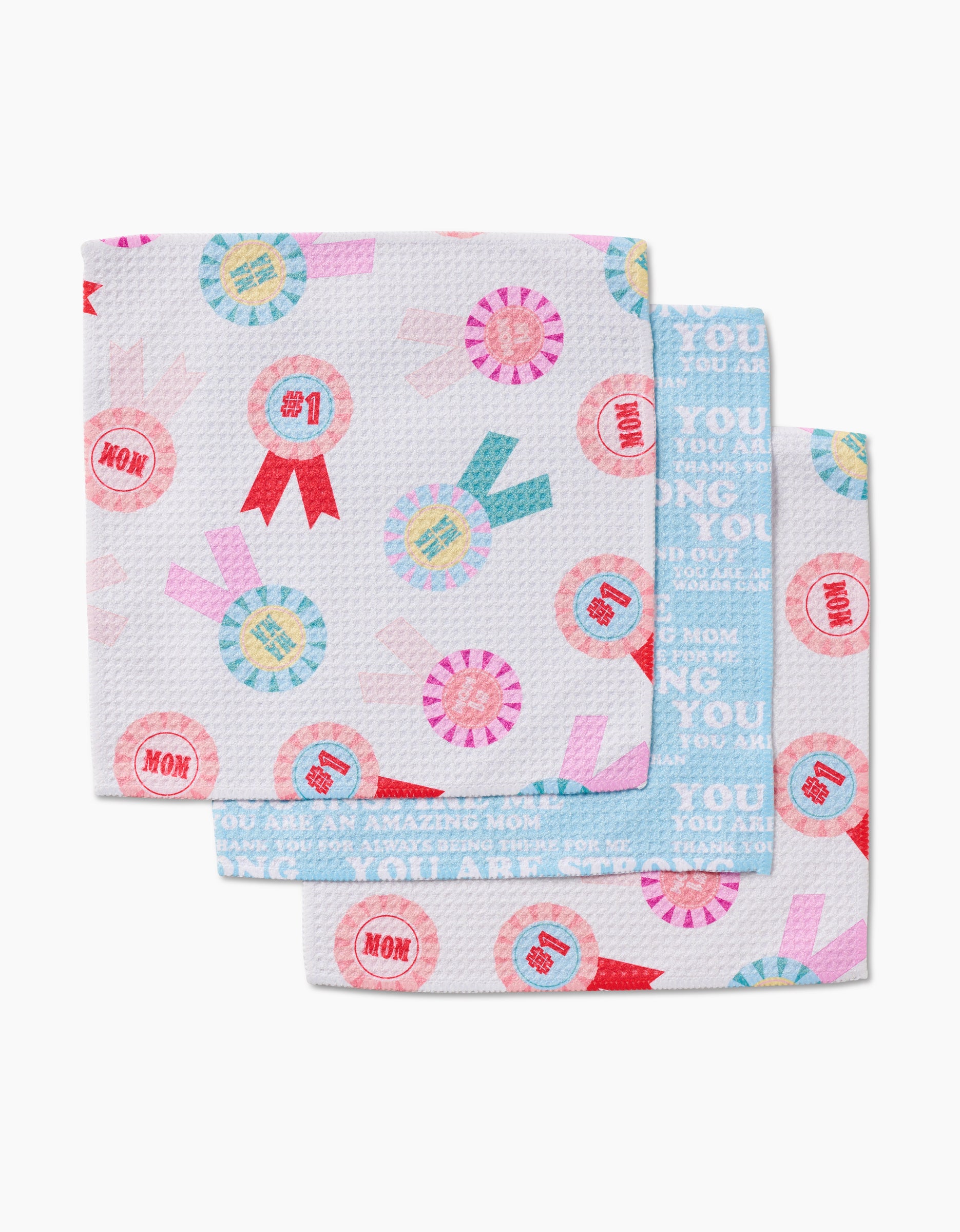 The GEOMETRY Mom Mantra Geoweave dishcloth set includes three recycled, patterned cloths with colorful ribbons and phrases like #1 and MOM on white and blue backgrounds—perfect for celebrating mothers.