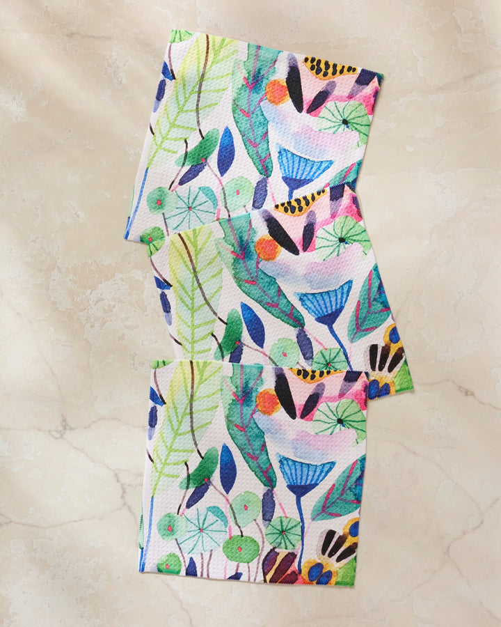 Three "Morning" napkins by Maria Montiel, made from recycled materials, feature a lively nature-inspired design with leaves, flowers, berries, and birds displayed on a light marble surface.