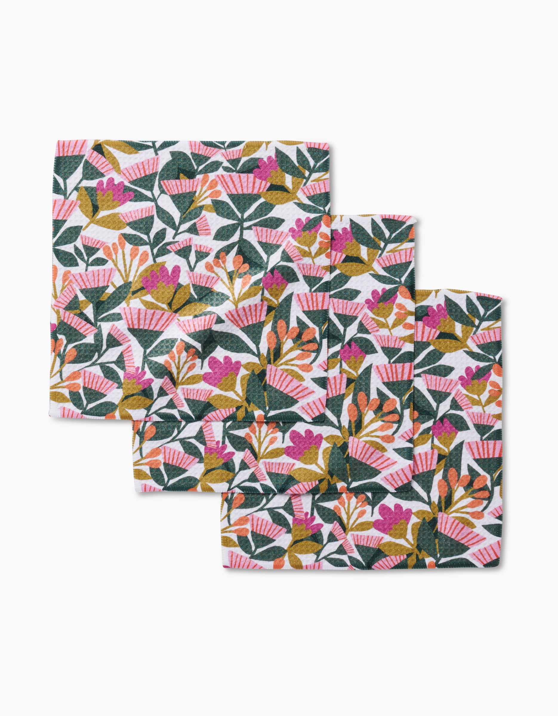 Three square Moxie Mauve dishcloths by Lisa Nelson with a floral pattern of green leaves and pink, orange, and yellow flowers, crafted from recycled materials, are arranged overlapping on a white background.