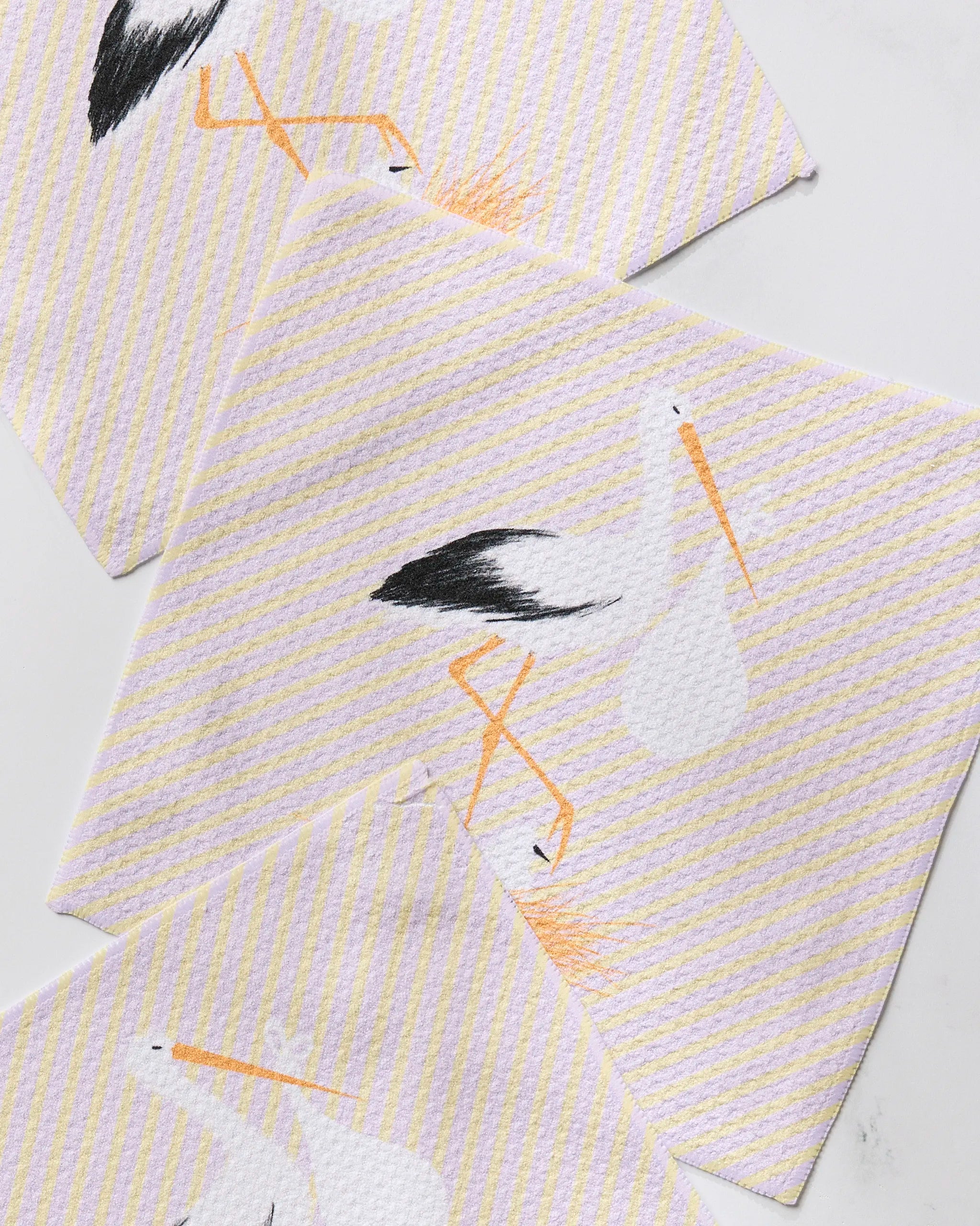 The Geometry New Mom dishcloth set features three white cloths with yellow diagonal stripes and a stork holding a bundle, made from recycled materials for super absorbency, neatly displayed on a white surface.