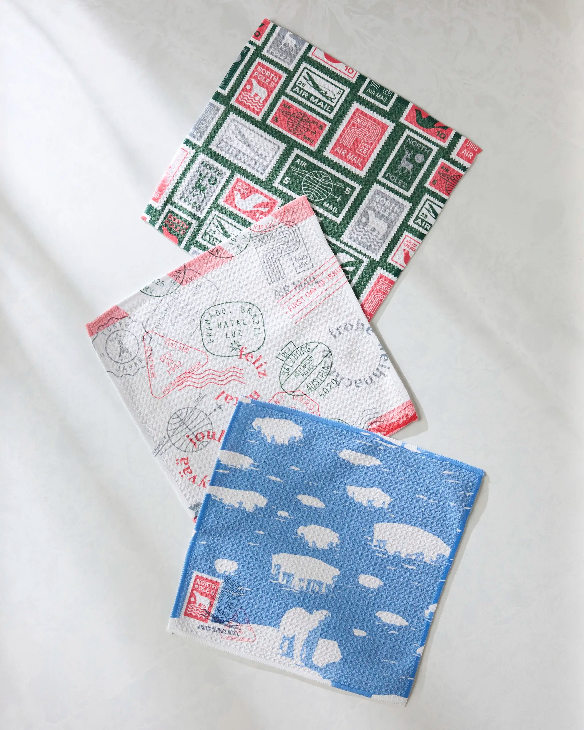Geometry’s Nordic Cheer dishcloth set features three vibrant designs—green and red stamps, red and gray postal marks, and blue with white sheep—all made from recycled materials.