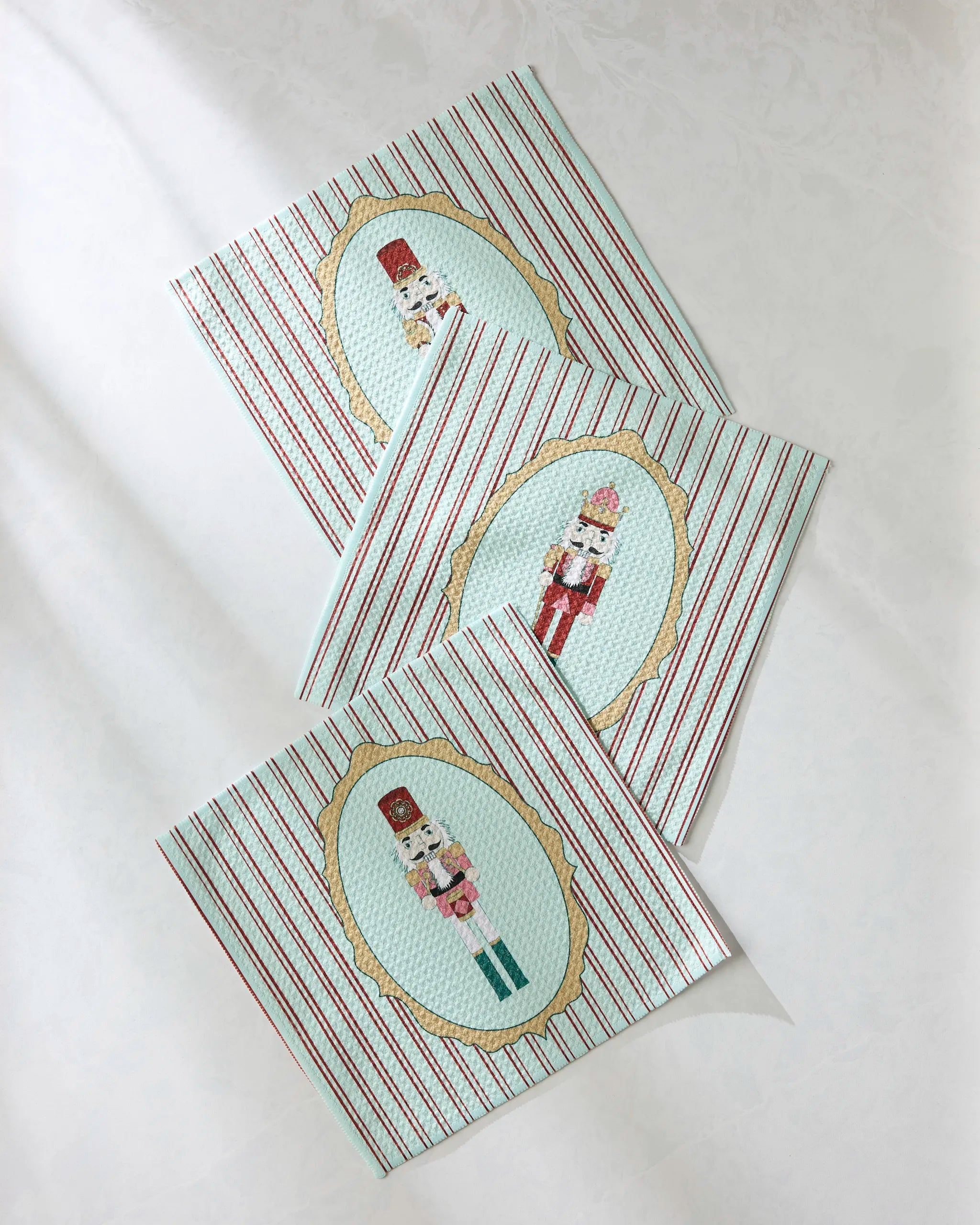 Three Nutcracker Intermission napkins by Geometry, featuring red and white stripes with a nutcracker design in the center, are displayed overlapping on a light surface—a festive addition to your dishcloth set.