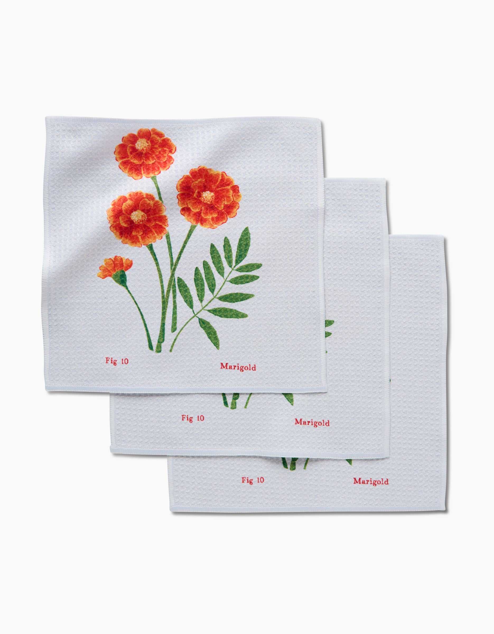 The October Marigold napkins by Linda Fox come in a set of three, made from white Geoweave fabric with orange marigold flowers, green leaves, and Fig 10 and Marigold printed in red on the corner.