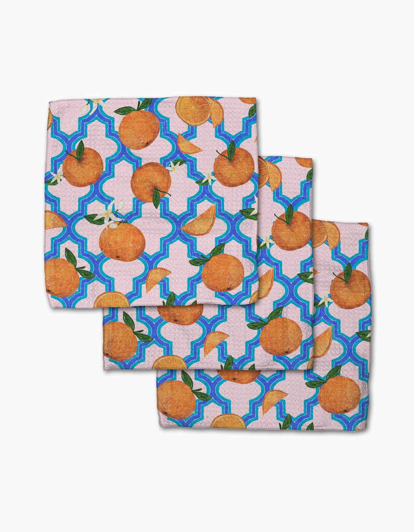 Three square cloth napkins from Pascale Dilger’s Orange Trellis collection, made of recycled materials, display vibrant oranges with green leaves and a blue trellis pattern on a light background, shown in an overlapping stack.