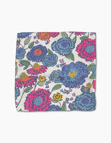The Painterly Meadow dishcloth by Kris Ruff features large pink, blue, and purple flowers with green leaves on a light background. Made from Geoweave fabric, it has a colorful floral pattern and a slightly textured appearance.