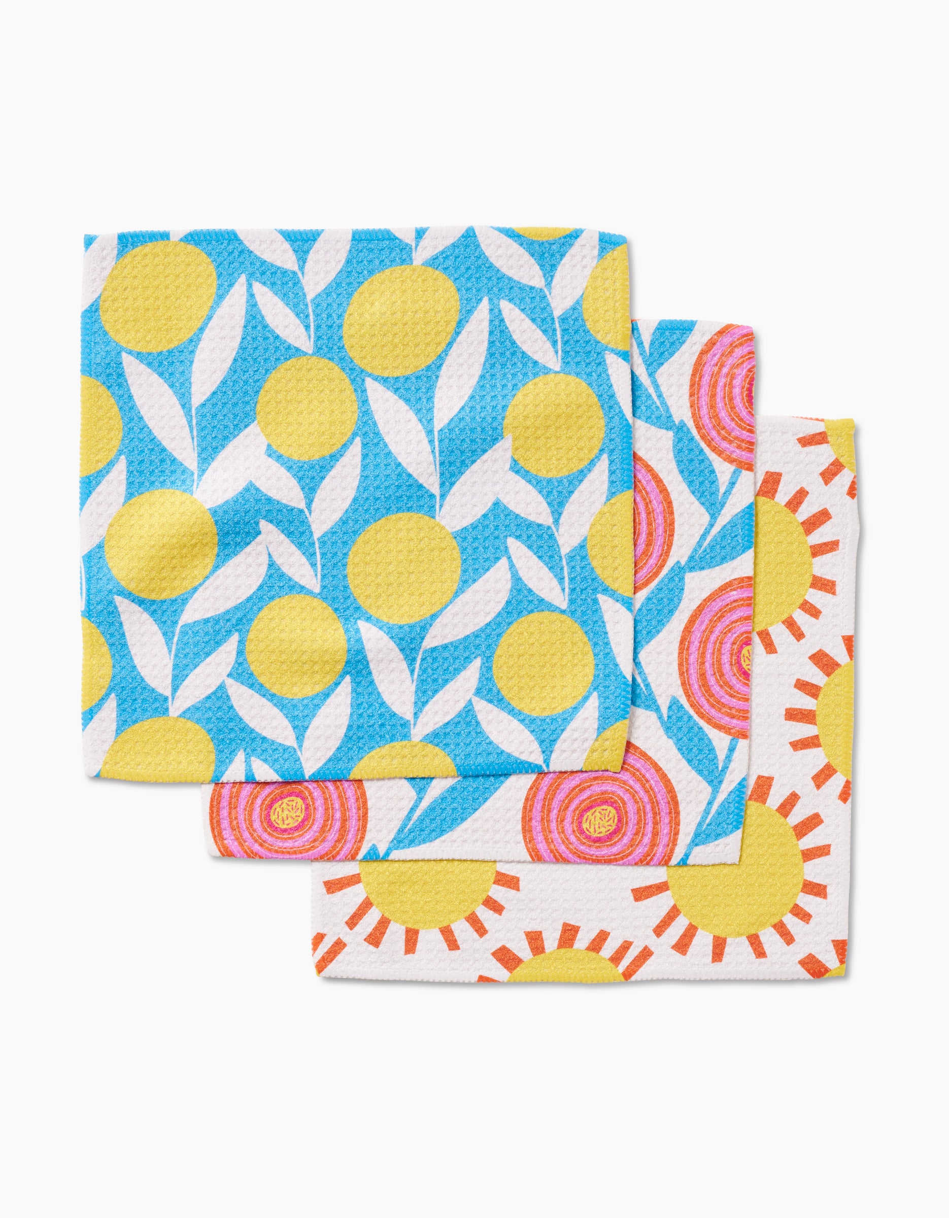 Three Parade dishcloths by Lizzie Clark are stacked, each made from Geoweave fabric and featuring vibrant sun-inspired designs in blue, yellow, pink, orange, and white. The top cloth highlights yellow circles and white leaves on blue.