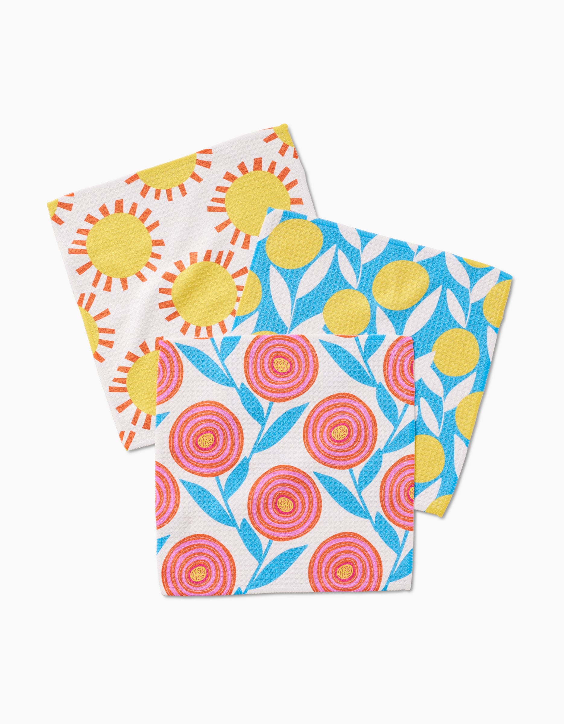 The Parade dishcloth set by Lizzie Clark features three vibrant Geoweave cloths: yellow suns with red rays, yellow circles with blue leaves, and pink circular flowers, all on white backgrounds.