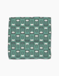 The Park Lane dishcloth by Charlie Rowan Designs is green with a grid of white flowers, stems, and leaves on a darker green background. Made from super-absorbent Geoweave fabric for efficient cleaning.
