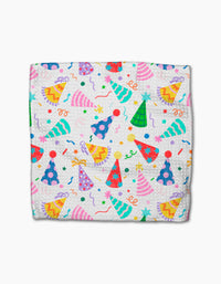 Party Pop by Vaishali Design Studio is a folded white blanket made from eco-friendly Geoweave fabric, featuring pink, blue, green, and yellow party hats with stars, confetti, and streamers scattered across the surface.