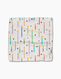 The Party Pop dishcloth by Vaishali Design Studio features a white textured Geoweave fabric with vibrant birthday candles, black stars, and yellow flames. Eco-friendly and durable, its perfect for adding a festive touch to your kitchen.