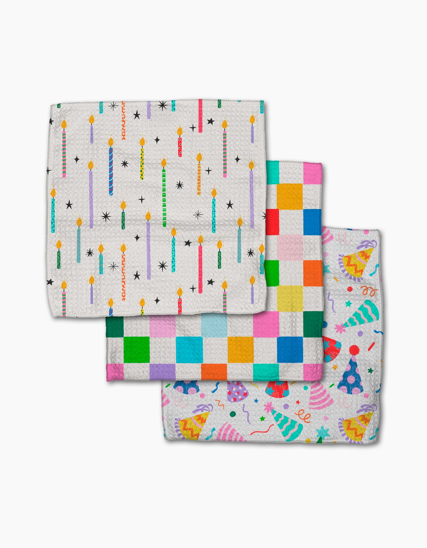 Three colorful Party Pop Geoweave cloths by Vaishali Design Studio are stacked: the top has birthday candles, the middle a multicolored check pattern, and the bottom shows party hats, cupcakes, and confetti on an eco-friendly white background.