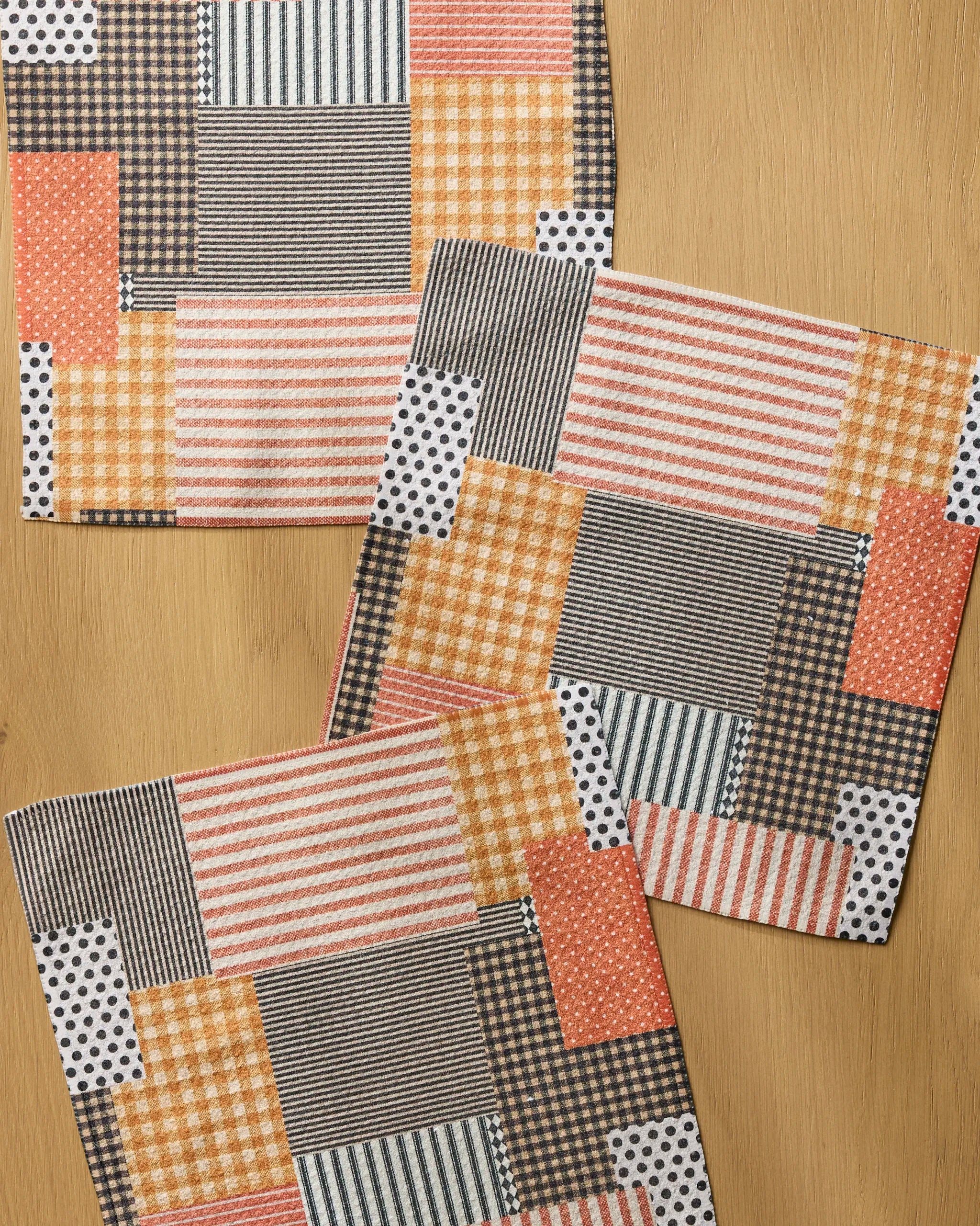 Geometry’s Patch and Pumpkin set includes three square placemats with a patchwork of stripes, gingham, polka dots, and checkerboards in orange, yellow, black, and white—perfect for a stylish and practical kitchen.