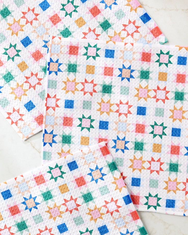 Four super-absorbent Patchwork Picnic dishtowels by Brittany Jepsen, featuring a colorful geometric star and square pattern in red, blue, green, and orange, made from recycled materials and displayed on a light surface.