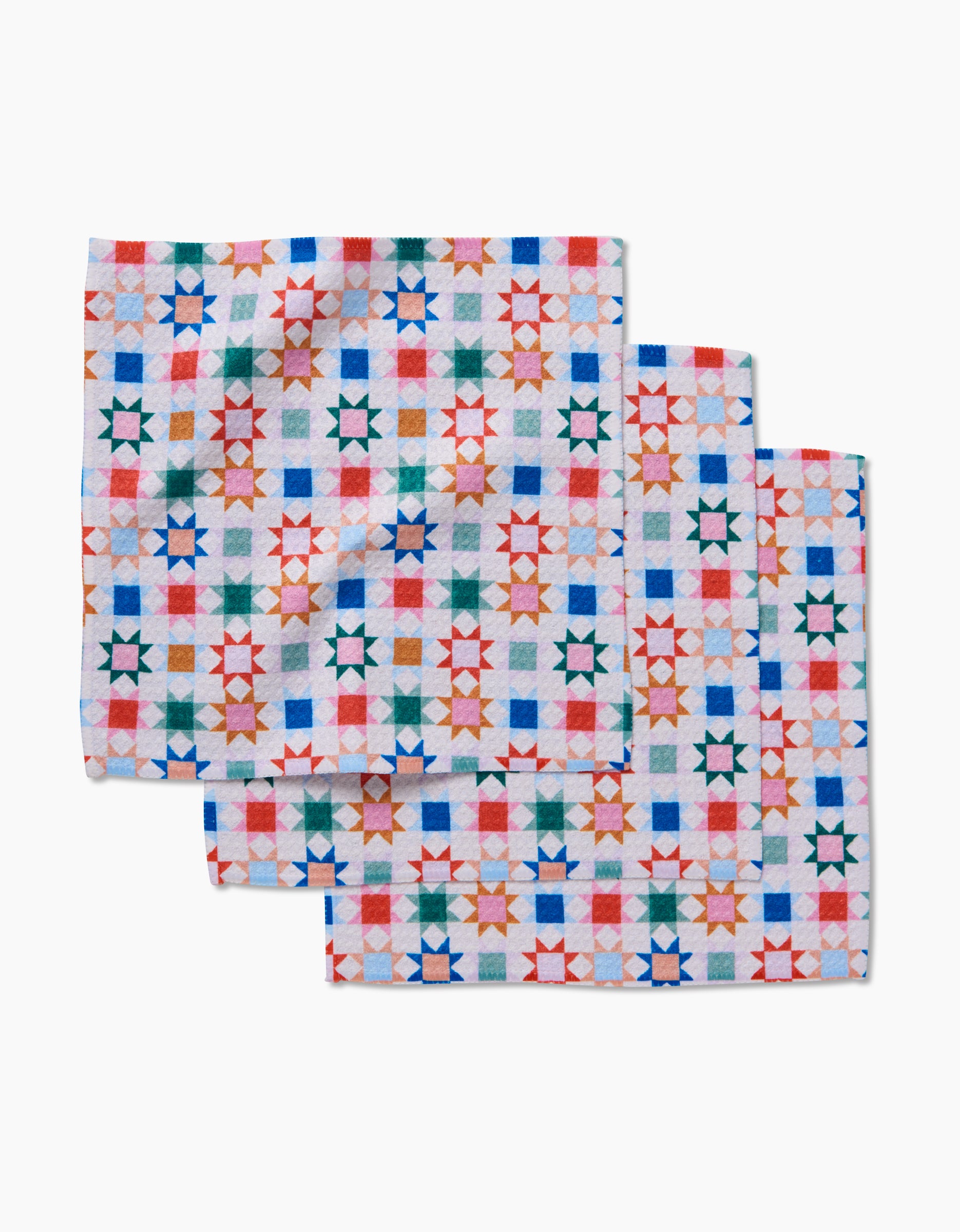 Three Patchwork Picnic cloth napkins by Brittany Jepsen, made from Geoweave fabric, display a colorful geometric star and square design in red, green, blue, and orange on white. They’re arranged with slight overlap on a plain surface.