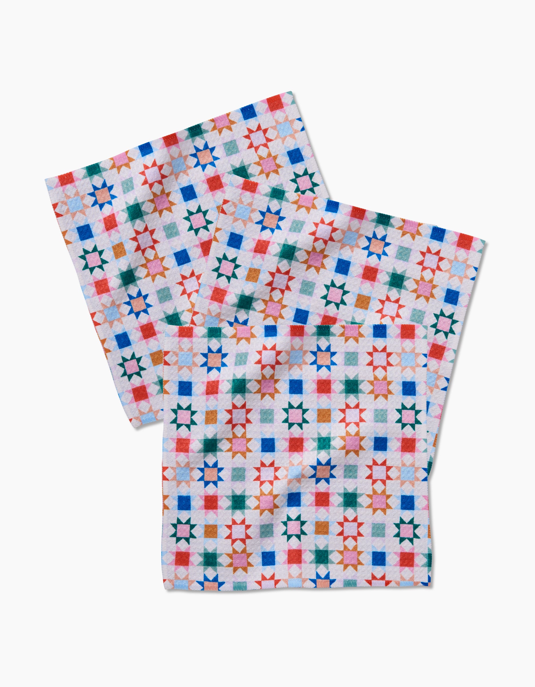 The Patchwork Picnic napkins by Brittany Jepsen are white Geoweave cloths, each featuring a grid of colorful stars and squares in red, blue, green, and orange on a plain background.