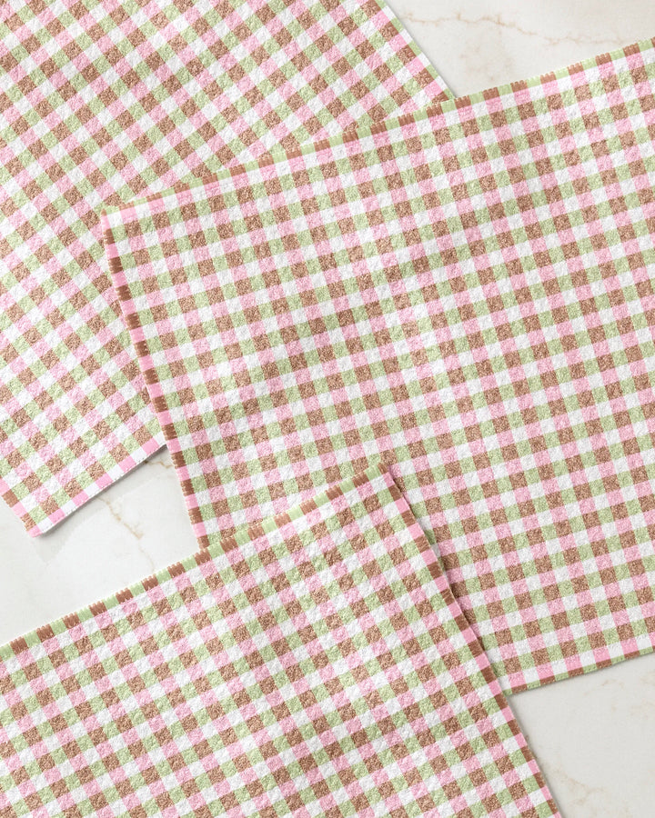 Three Patricia Plaid placemats by Laura Prietto, featuring a pink, brown, and white gingham pattern, are arranged on a marble surface. Made from recycled materials for an eco-friendly touch.